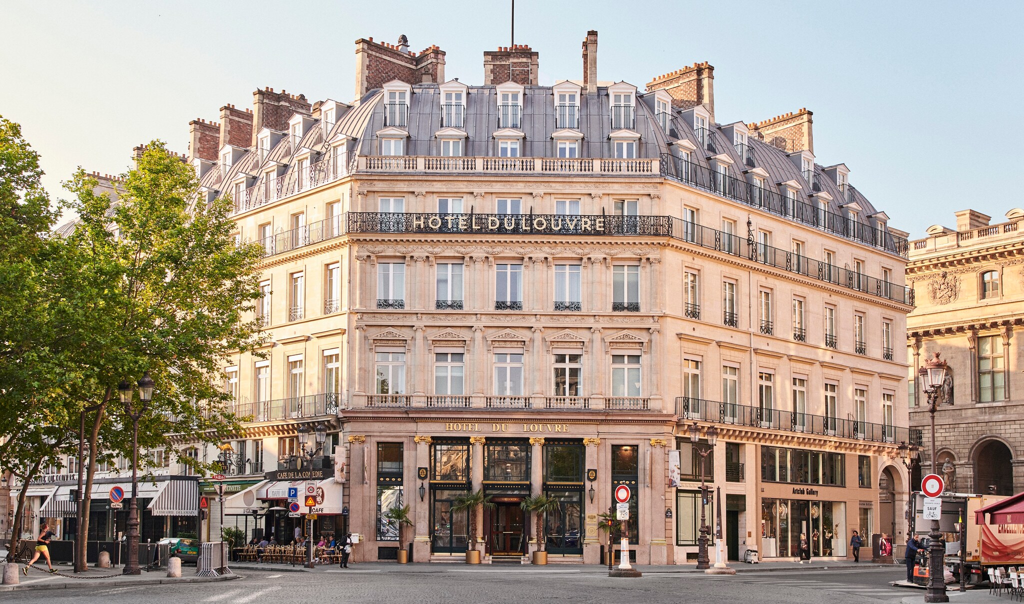 An exterior view of the hotel shows a grand building with Haussmann-style architecture situated on a city street corner.