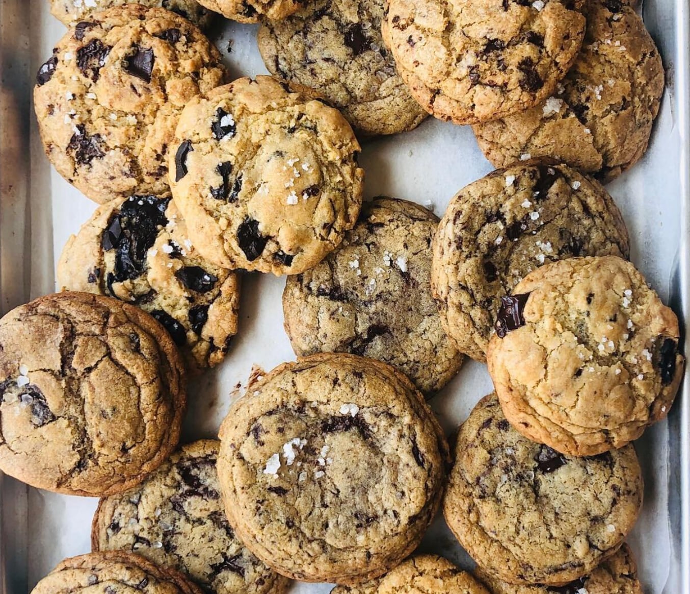 Overhead view of a tray of chocolate chip cookies sprinkled with chunky salt.