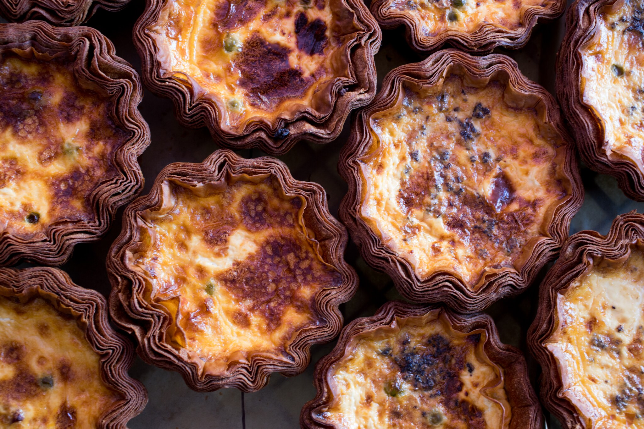Overhead view of many quiches clustered together, all with scalloped, many-layered brown crusts.