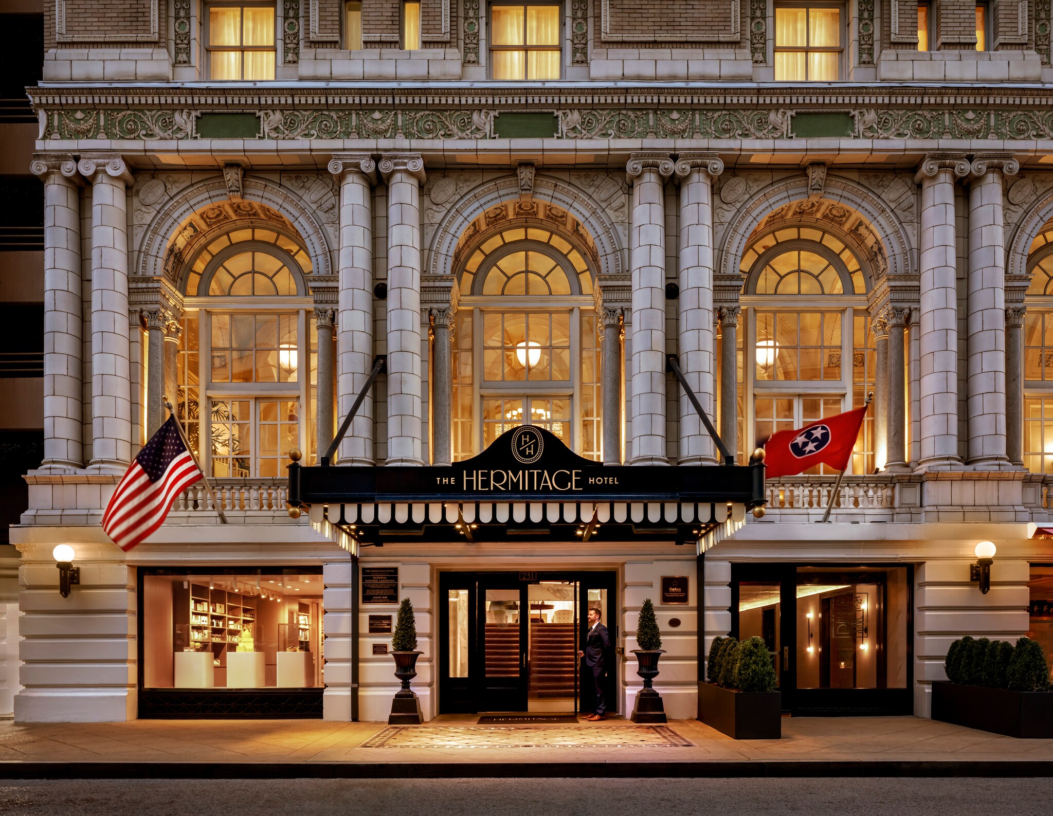 Exterior of The Hermitage Hotel, which has a white front with black accents and is flying the flags for the United States and Tennessee.