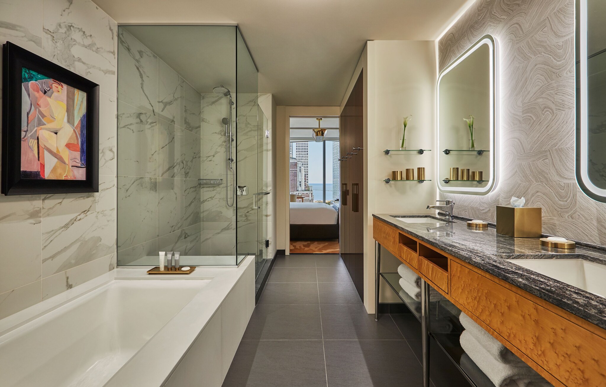 The bathroom of a Grand Lakeview King has marble walls, dual vanities with backlit mirrors, a deep soaking tub, and a large walk-in shower.