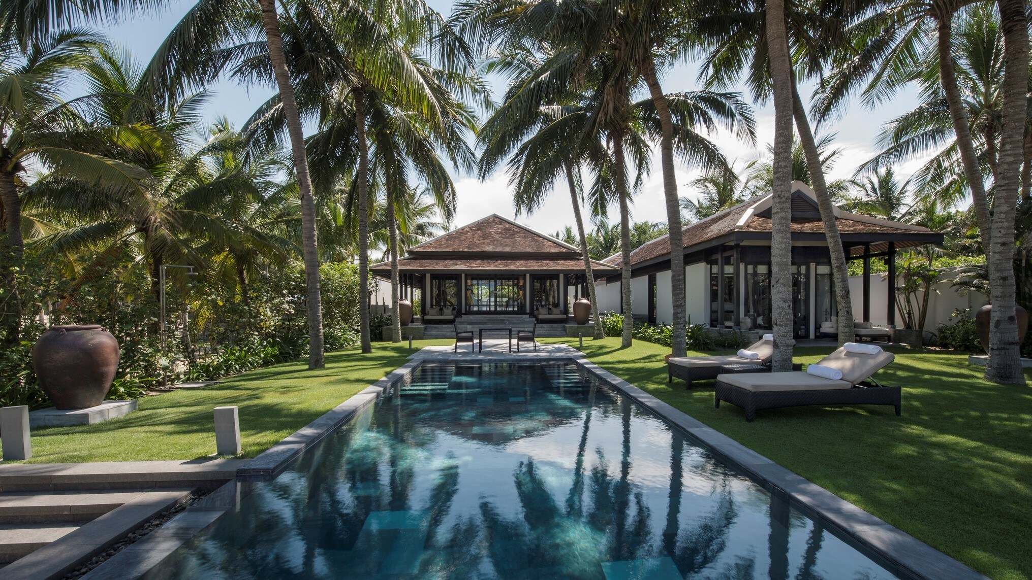 Exterior of the one-bedroom Pool Villa, which features a long, rectangular pool surrounded by grass and palm trees.