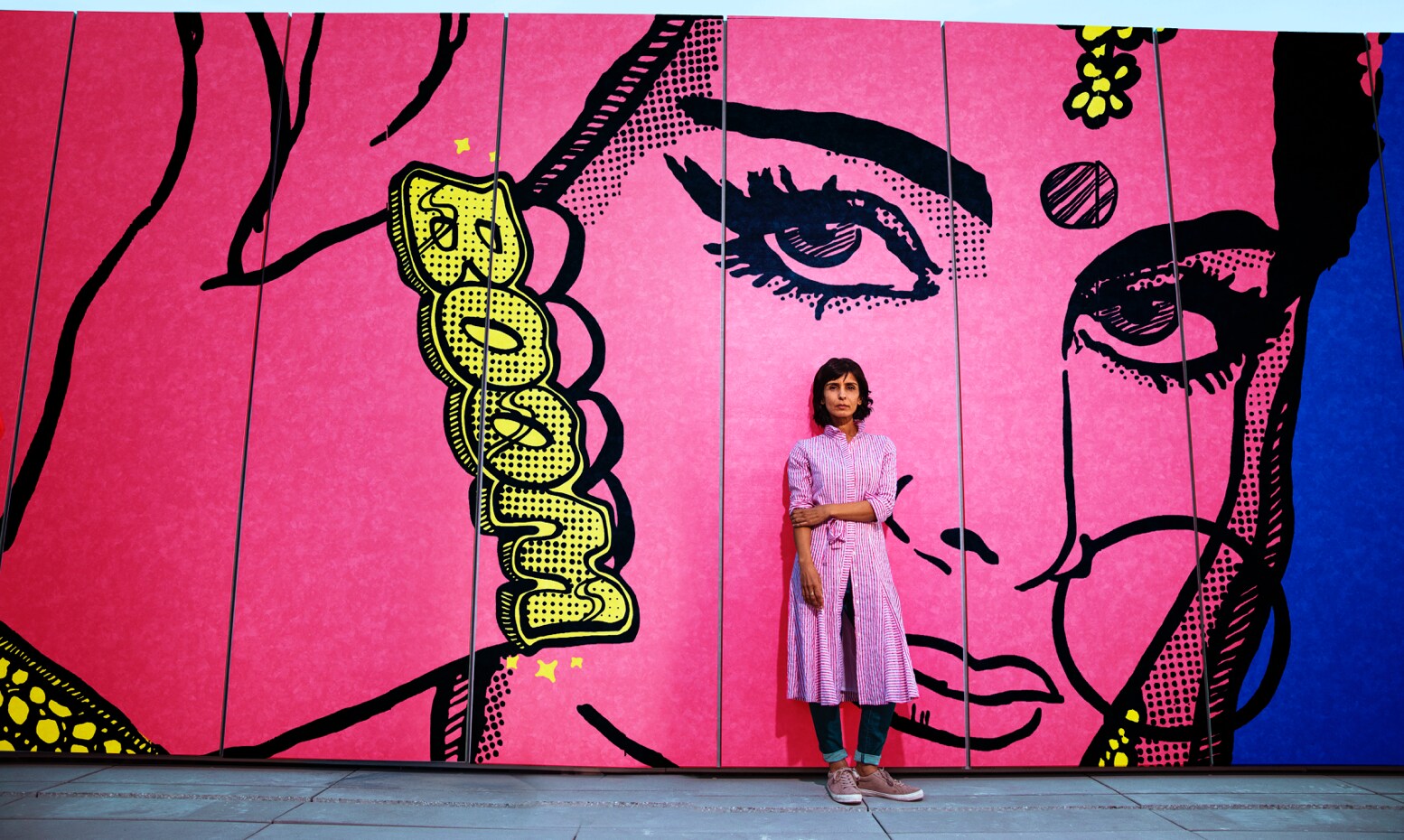 Artist Jas Charanjiva stands in front of her Don’t Mess with Me mural, in which a pink Indian woman wears a gold knuckle piece reading BOOM.