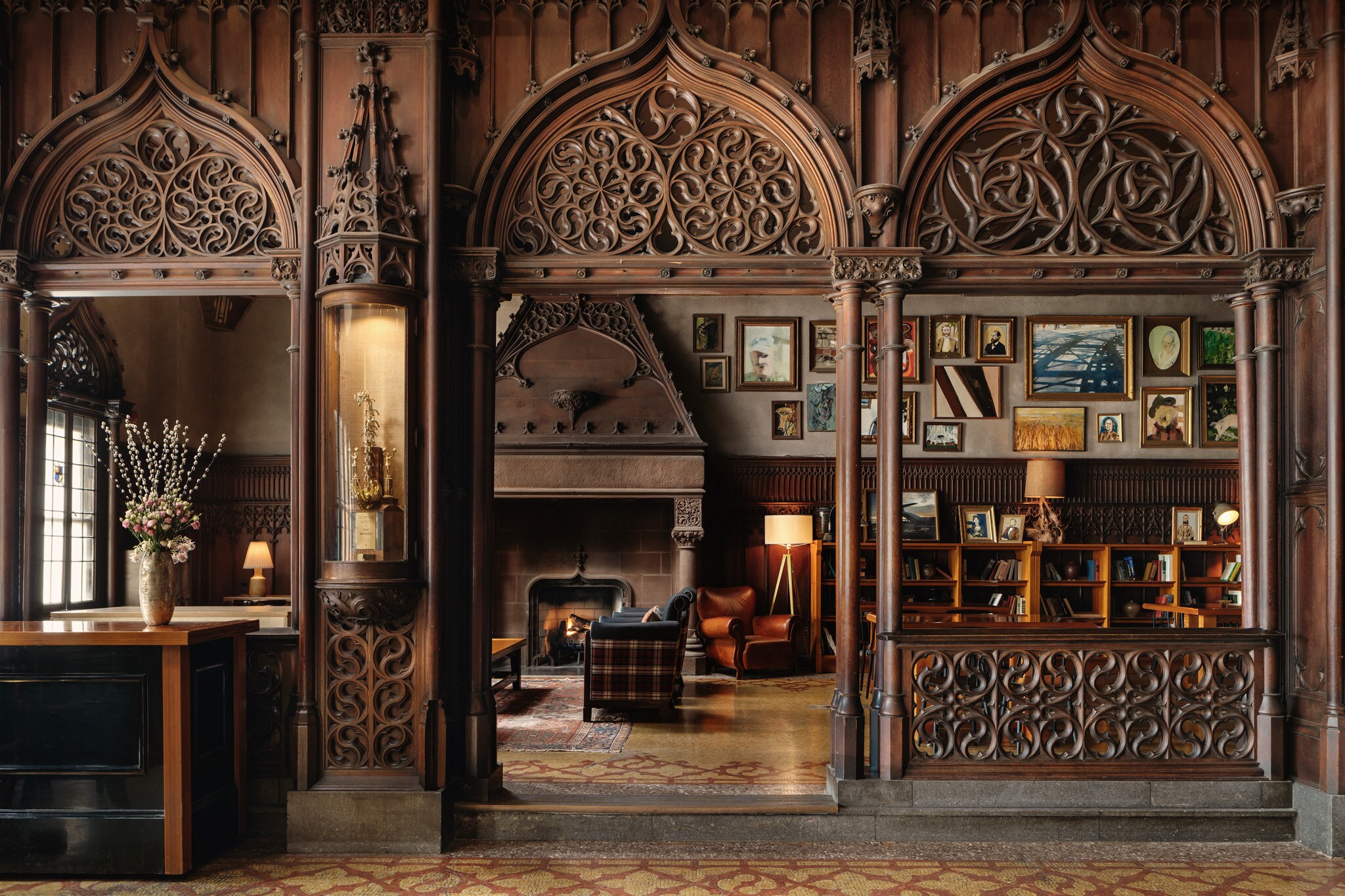 Elaborately carved dark wood panels frame the Drawing Room, which is filled with books, artwork, and furniture in leather and plaid.