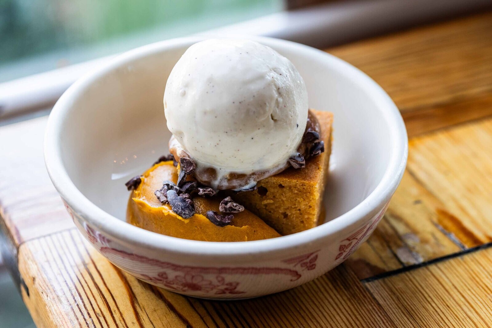 Close-up of a dessert, a baked square with curls of chocolate, a dollop of an orange cream, and a scoop of ice cream atop it.