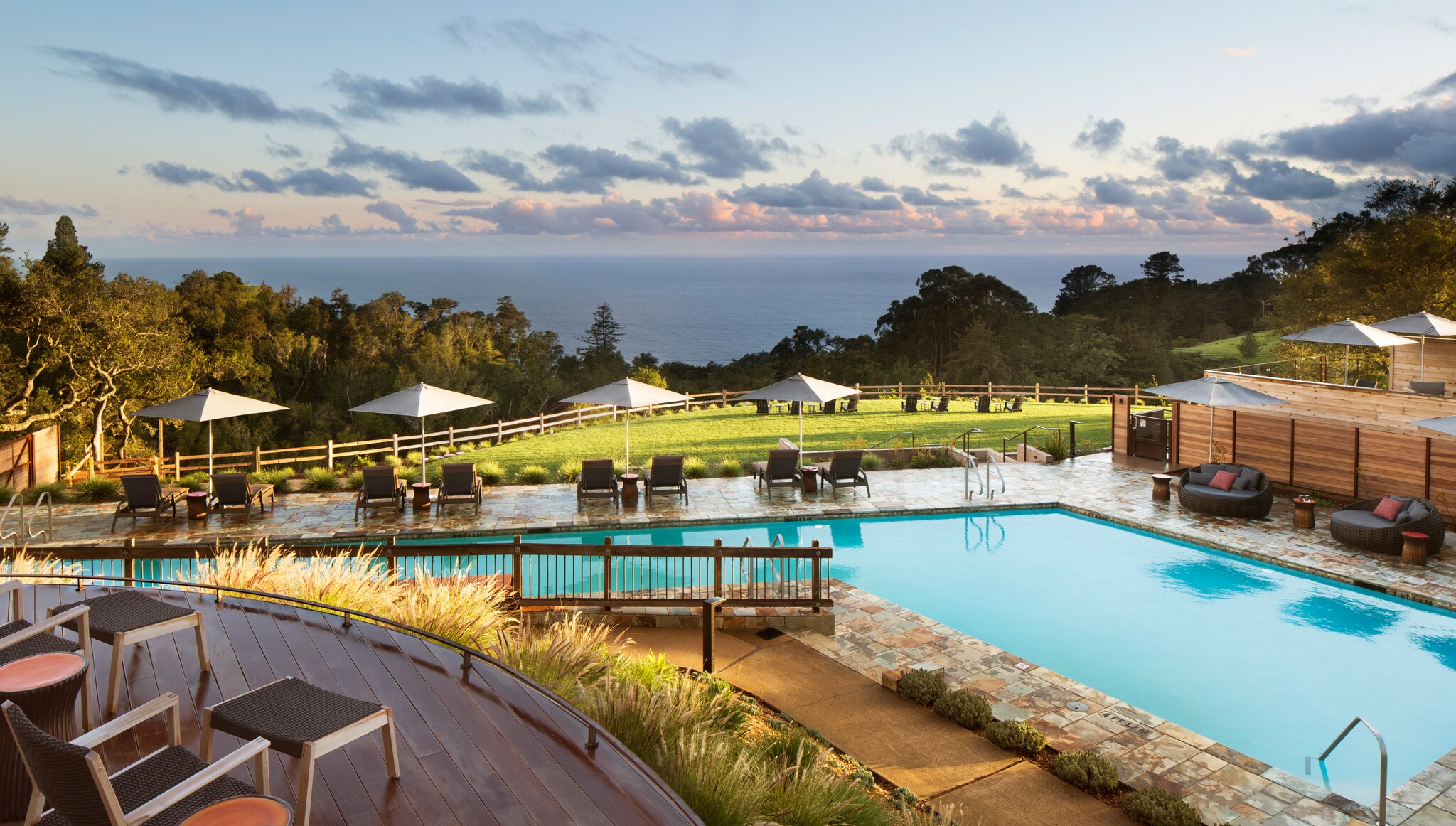 The deck of the main pool overlooks a wide lawn arrayed with chairs, and beyond a hill covered in trees gives way to the Pacific Ocean.