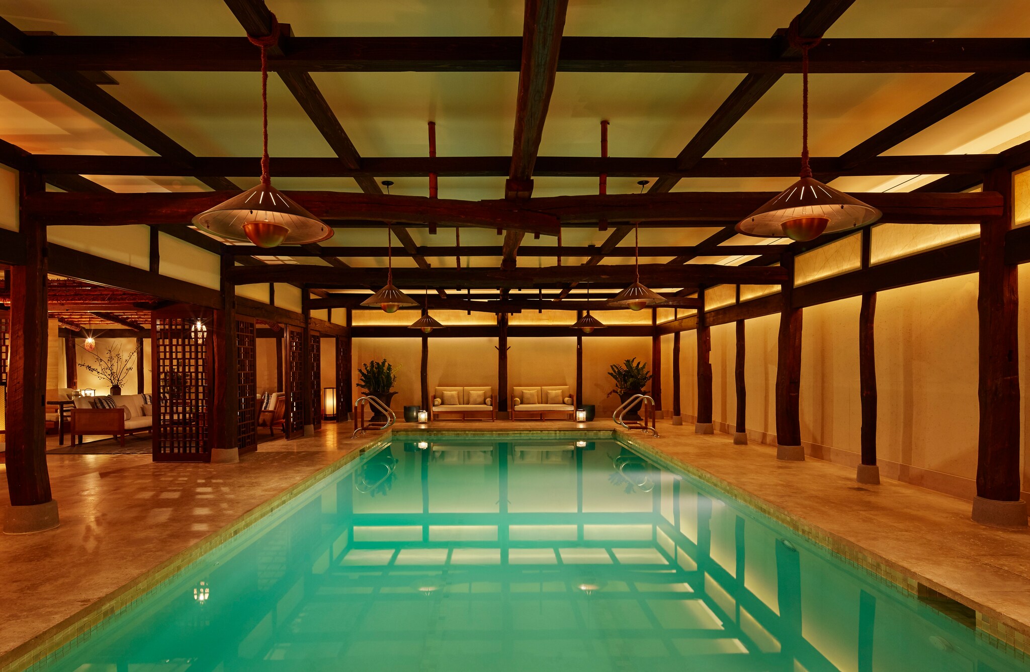 The Shibui Spa Pool is greenish in the light of the deep golden yellow of the surrounding spa, which has exposed beams and hanging lamps.