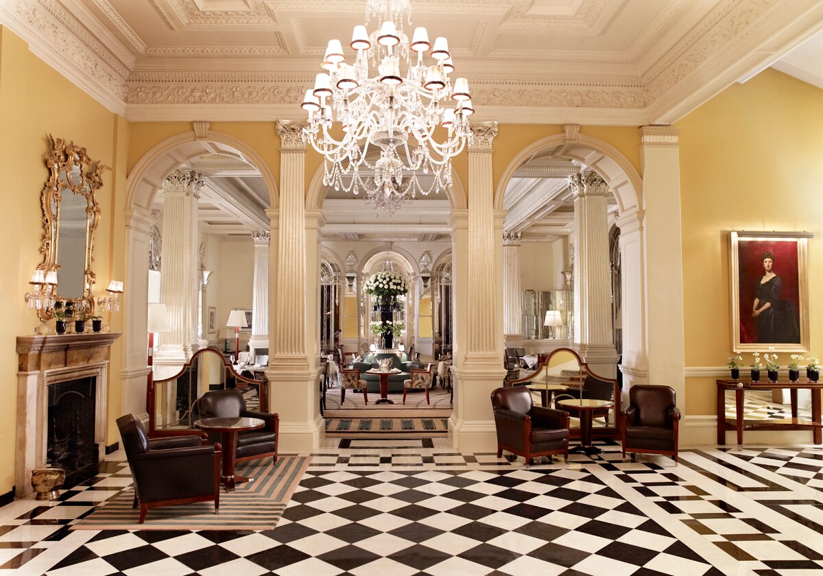 The lobby has black and white checkered tile floors, opulent chandeliers, neoclassical interior pillars, and ornate crown molding.