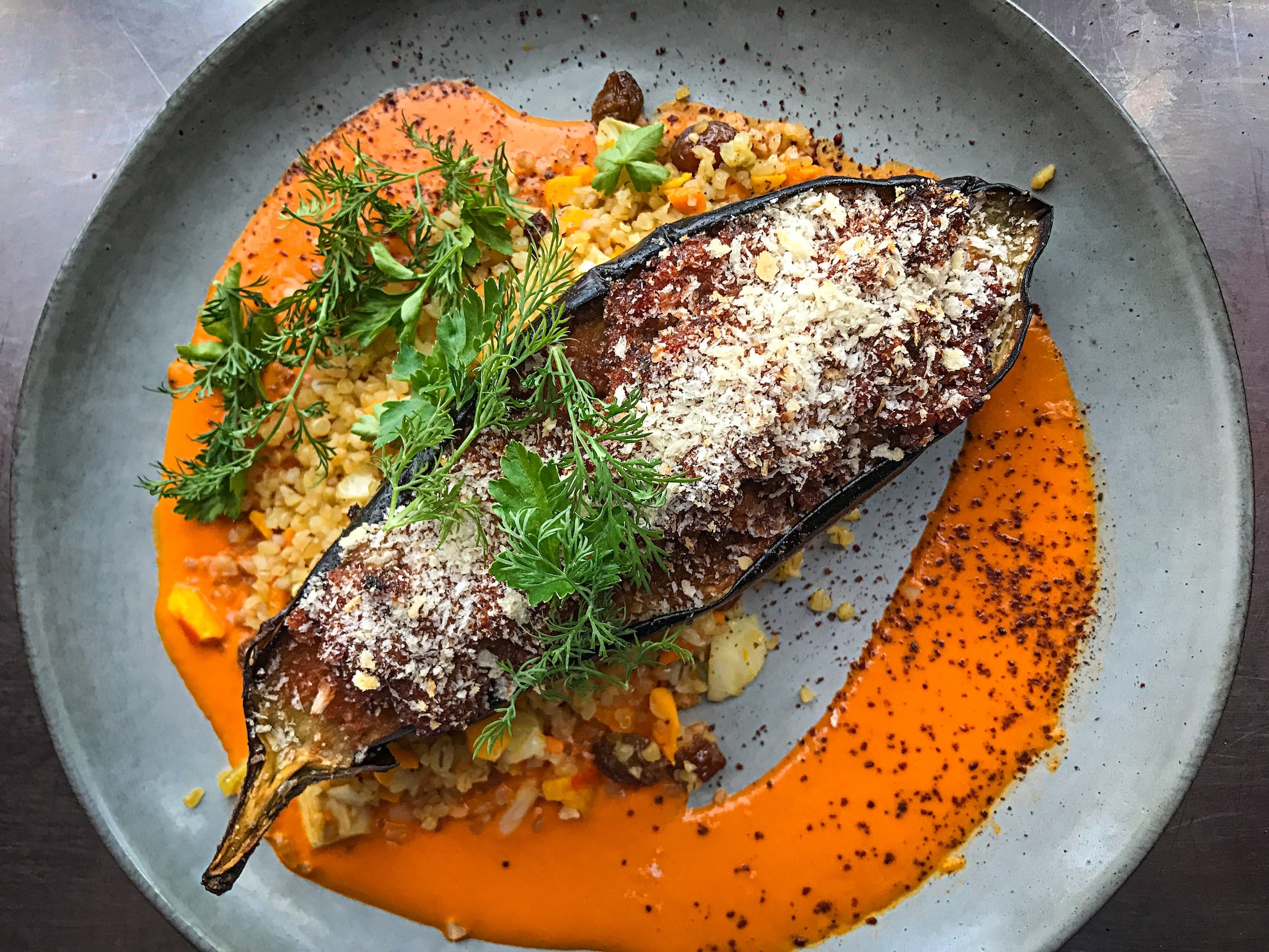 A lengthwise cross-section of eggplant is roasted and dusted with cheese and parsley. It rests on a bed of red sauce and minced vegetables.