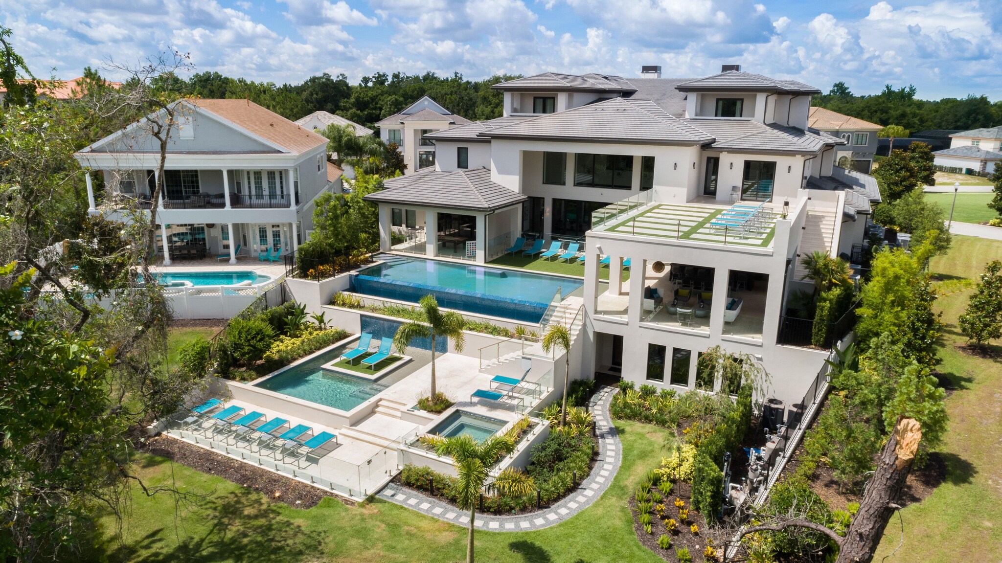 Aerial view of large two-story home with carriage house and expansive backyard featuring a multi-level swimming pool.
