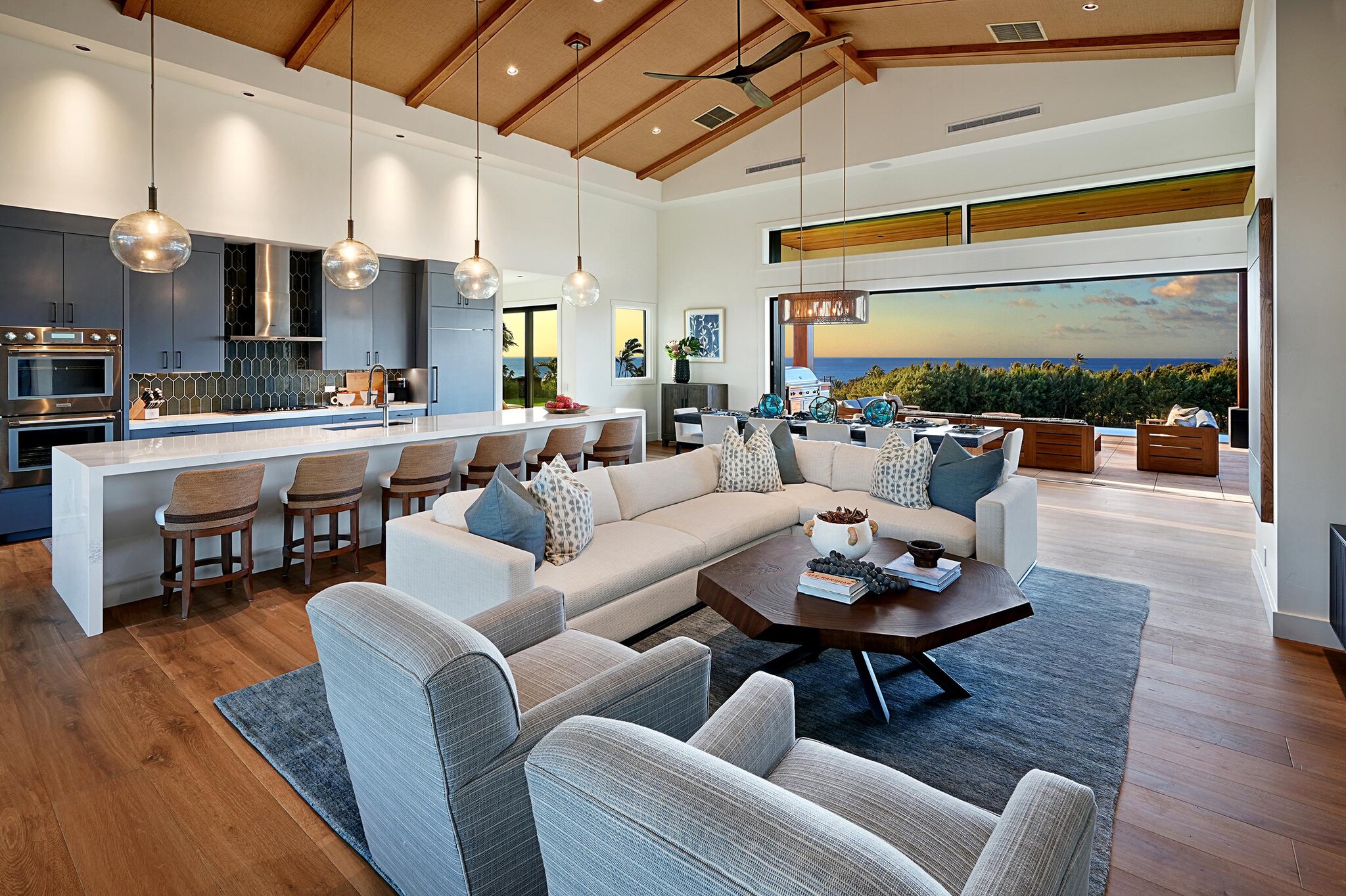 Interior of kitchen, dining, and living areas of house with view of the ocean through expansive bi-fold doors.