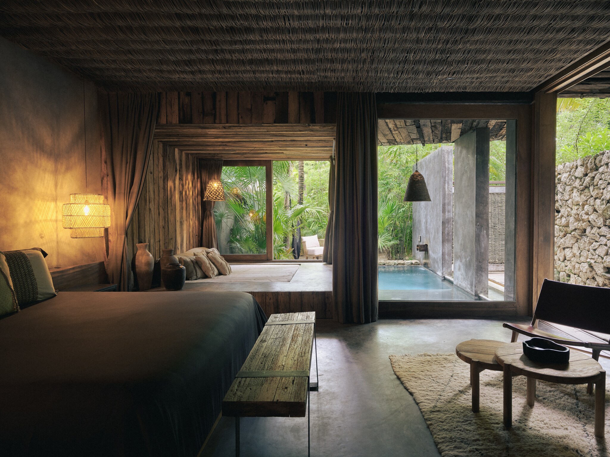 The Tierra Suite at Be Tulum has a woven roof and earth tones throughout the sleeping area and patio. A plunge pool adjoins dense greenery.