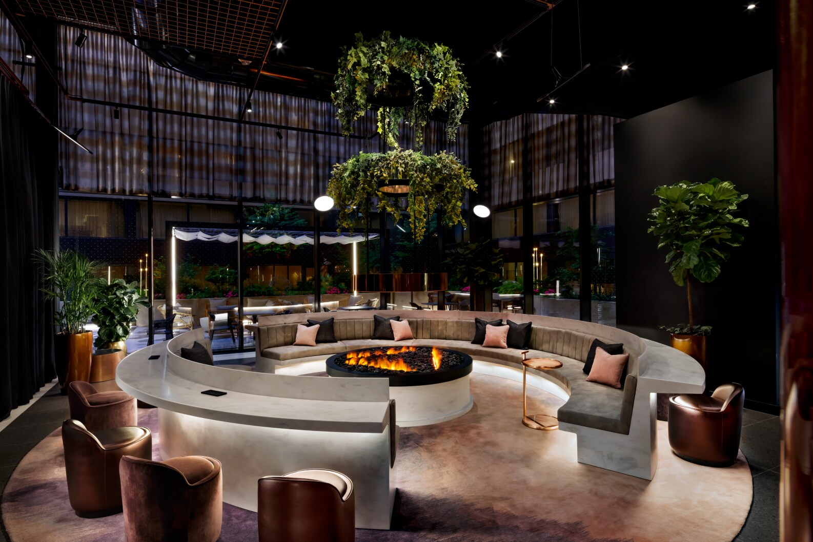 In the Living Room at W Toronto Hotel, circular gray counters and couches surround an indoor fire pit. Plants hang over the light fixtures.
