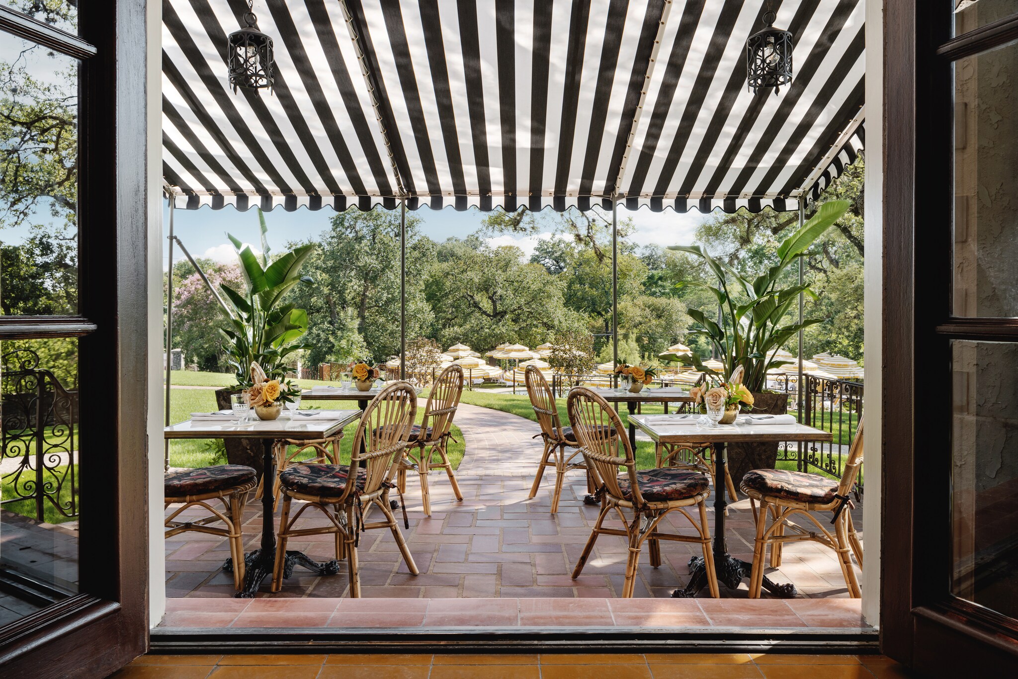 The terrace at Lutie's Garden Features a striped awning, wicker chairs, and potted plants overlooking the grounds.