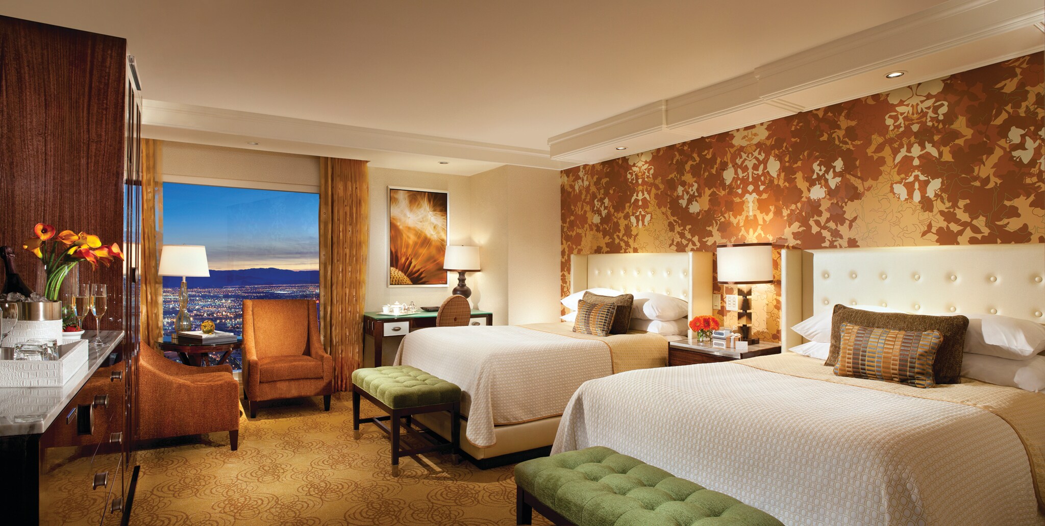 A room in the Bellagio has two queen-sized beds with large headboards. Armchairs are situated in front of a window overlooking the city.