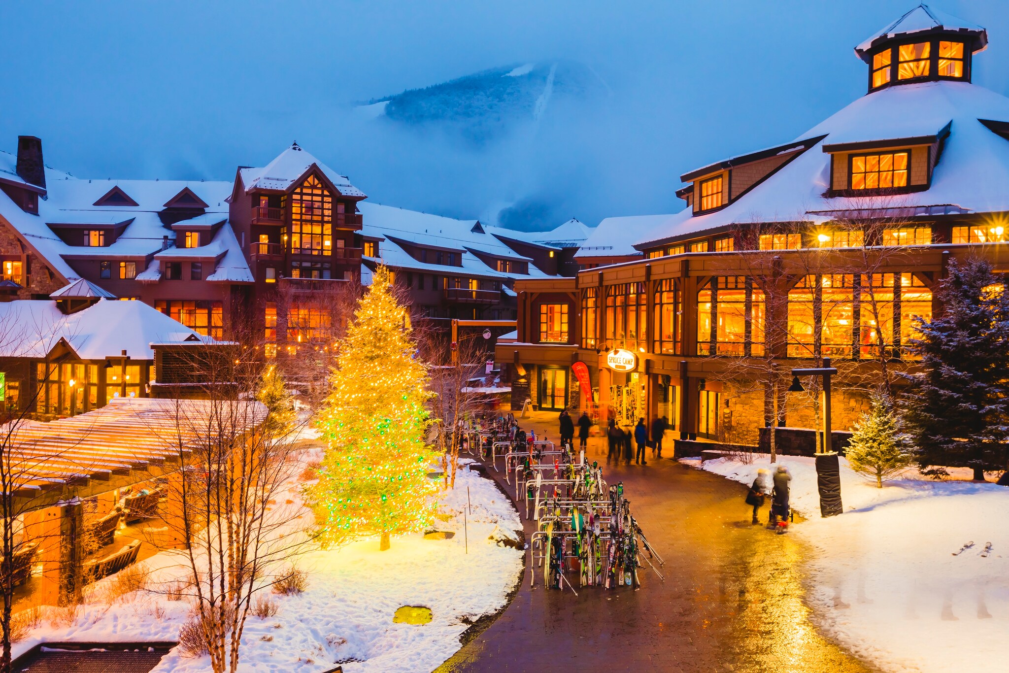 On a snowy evening, the hotel windows glow orange, and along with a lit Christmas tree they illuminate wide pathways thronged with people. 