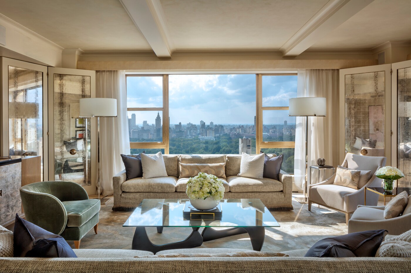  The living room of the Presidential Suite has large windows overlooking Central Park. Two gray couches surround a glass coffee table.