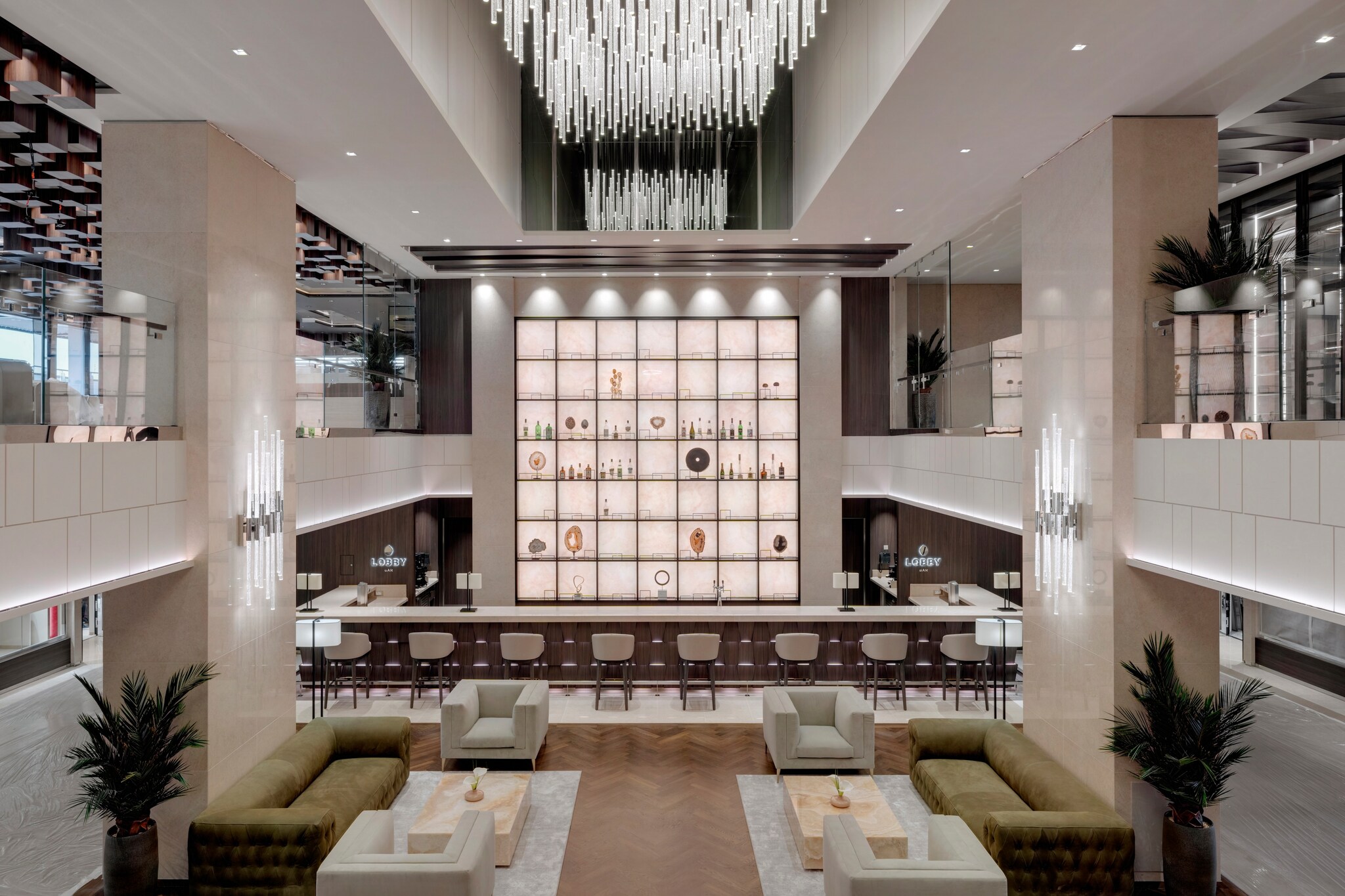 In the lobby of Explora I, a long white bar lined with chairs surrounds a large backlit grid of vases and sculptures on shelves. 