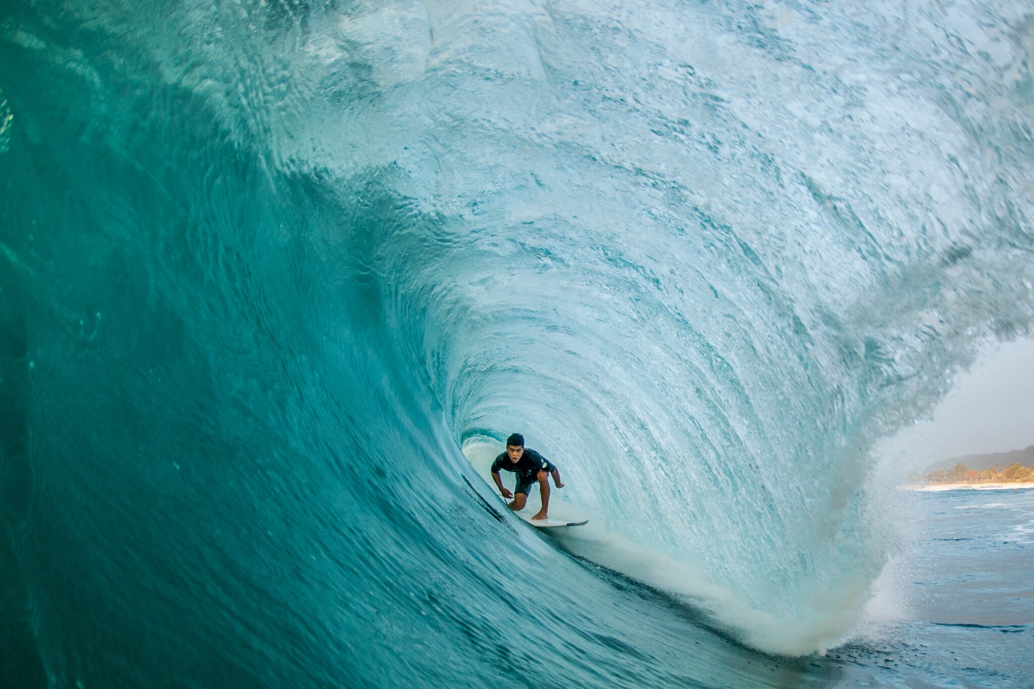 View inside the barrel of a wave as an Asian male surfer ducks down to surf through.