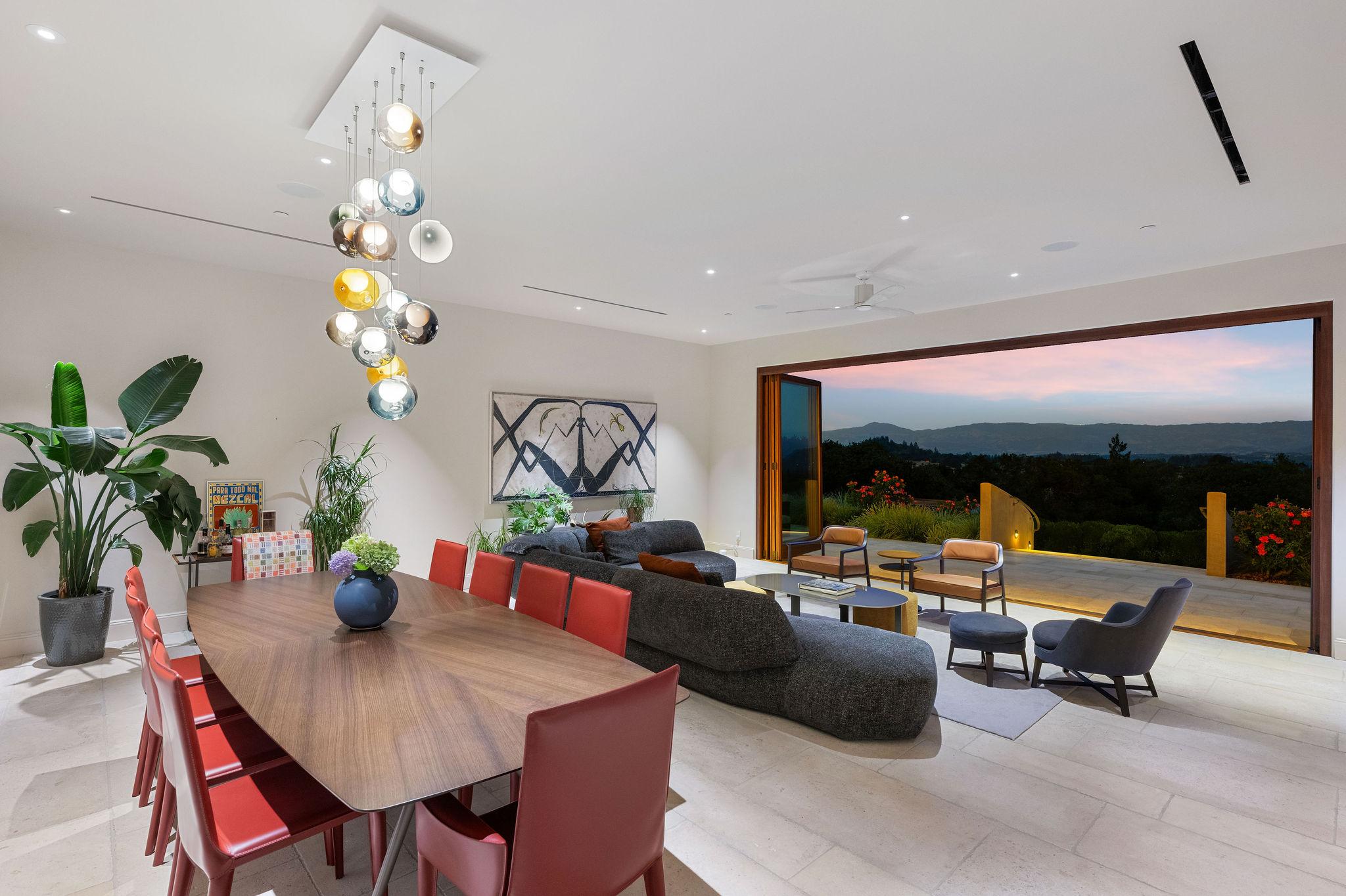 Interior view of living and dining areas highlighting view of the patio, countryside, and mountains at dusk through expansive bi-fold doors