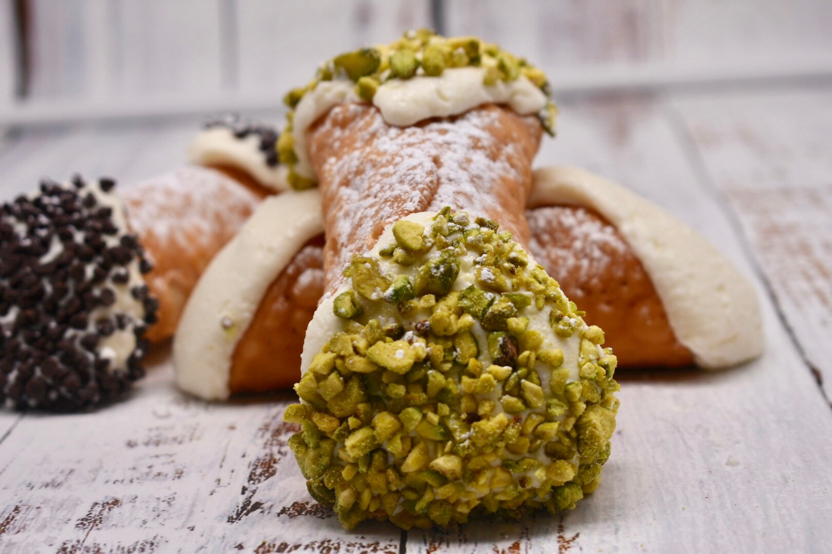 Close-up view of a pistachio cannoli propped up on a plain cannoli, with a chocolate cannoli just behind.