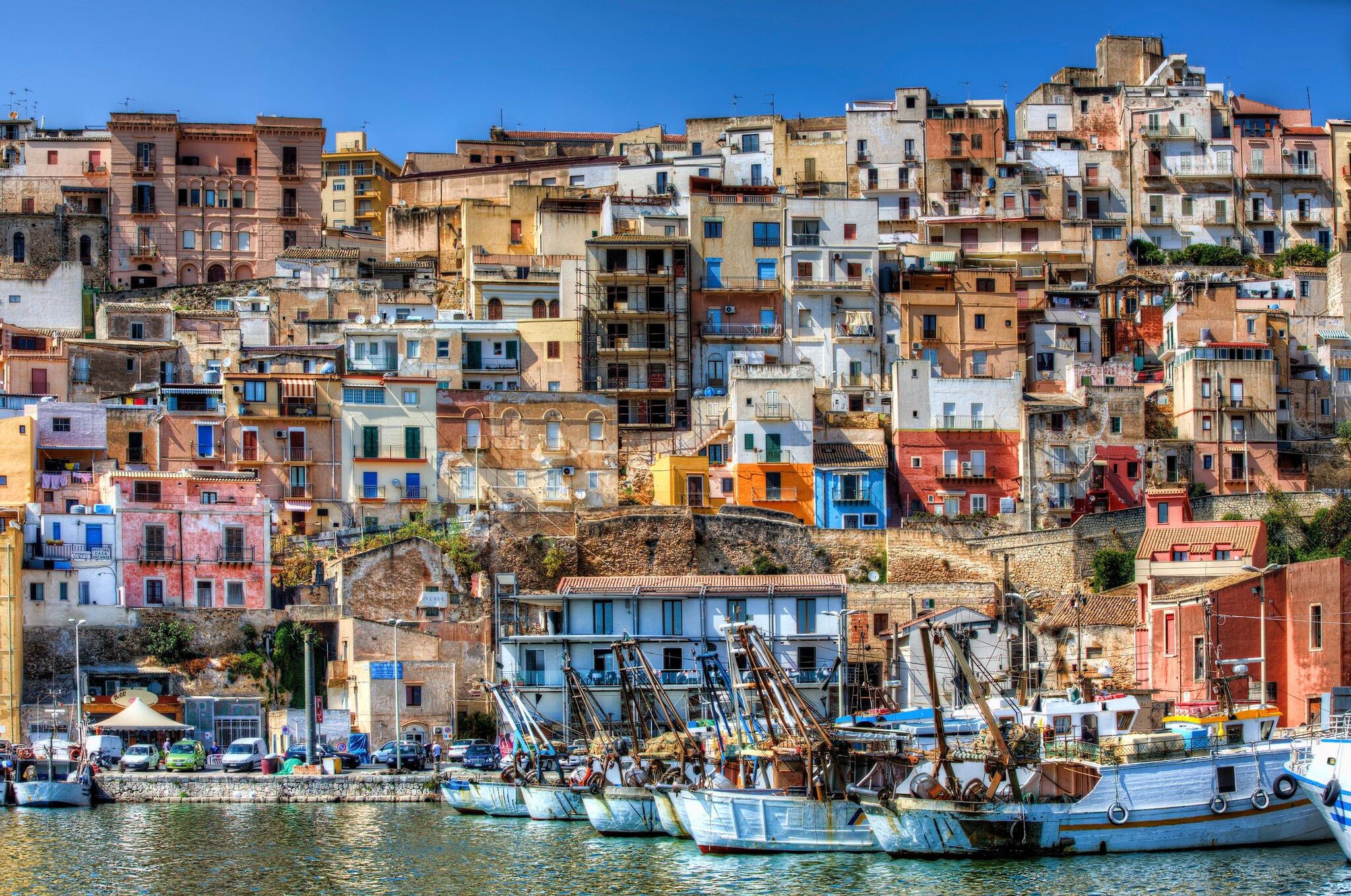 View from the water towards Sciacca, which winds up a steep hillside and is densely packed with narrow two-and-three story buildings.
