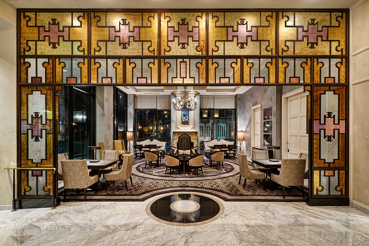 The lobby of Loews New Orleans has glossy marble floors, a gray-and-brown patterned carpet, and a stained-glass square arch.