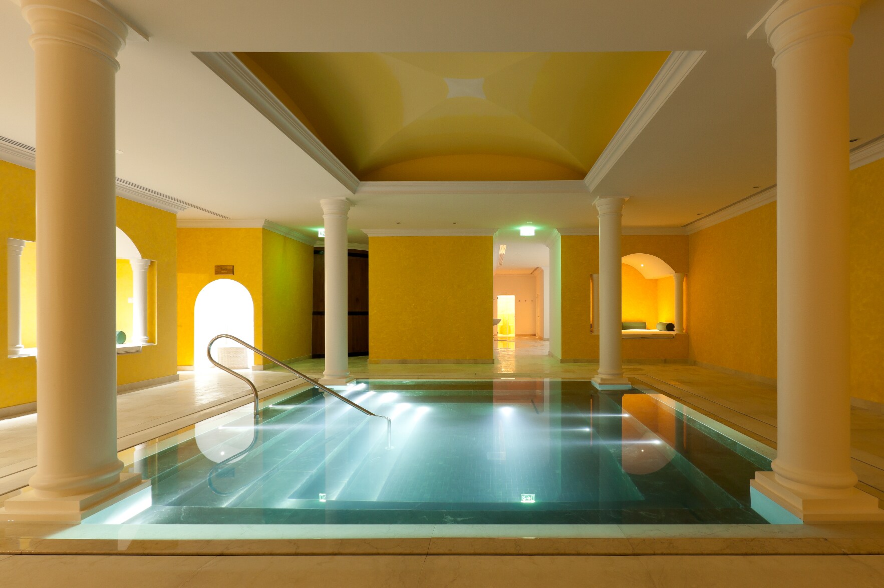 The spa’s Roman Bath has yellow walls with white columns and accents. The bath itself is square, with benches along the insides.
