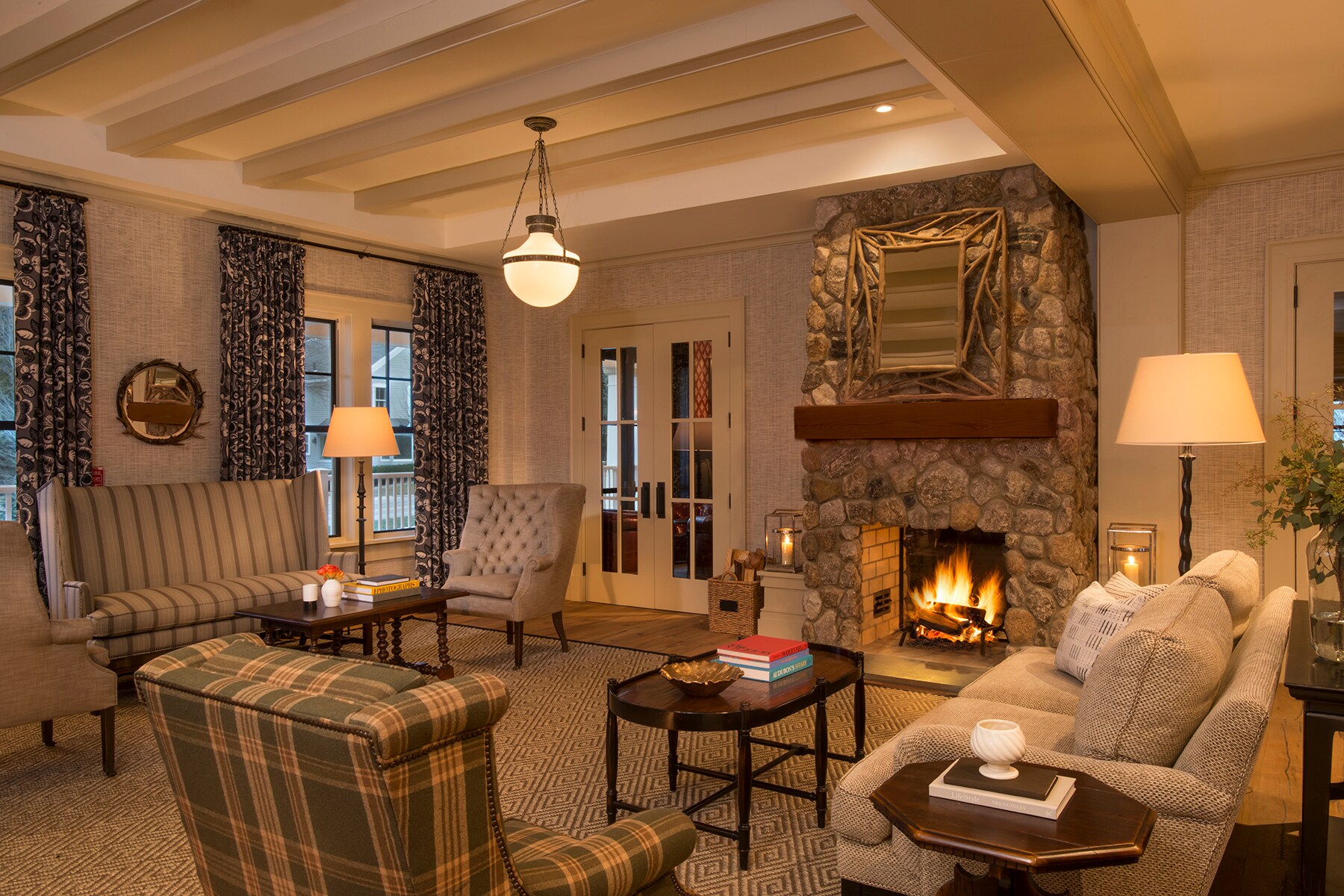 The living room at Kimpton Taconic Hotel has a lit stone fireplace, a mix of plush seating in tans and greens, and warm lamplight.