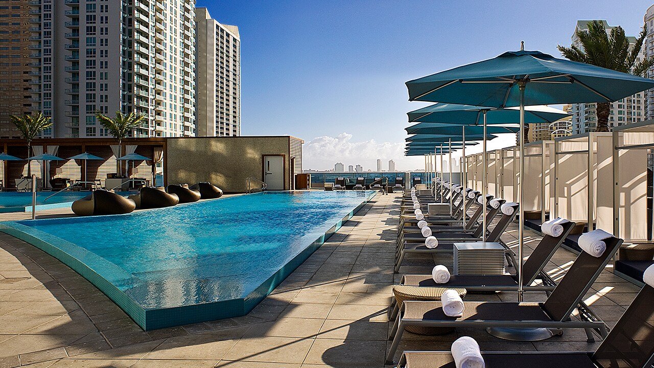 The irregularly-shaped outdoor pool is lined by long rows of sunbeds and umbrellas.