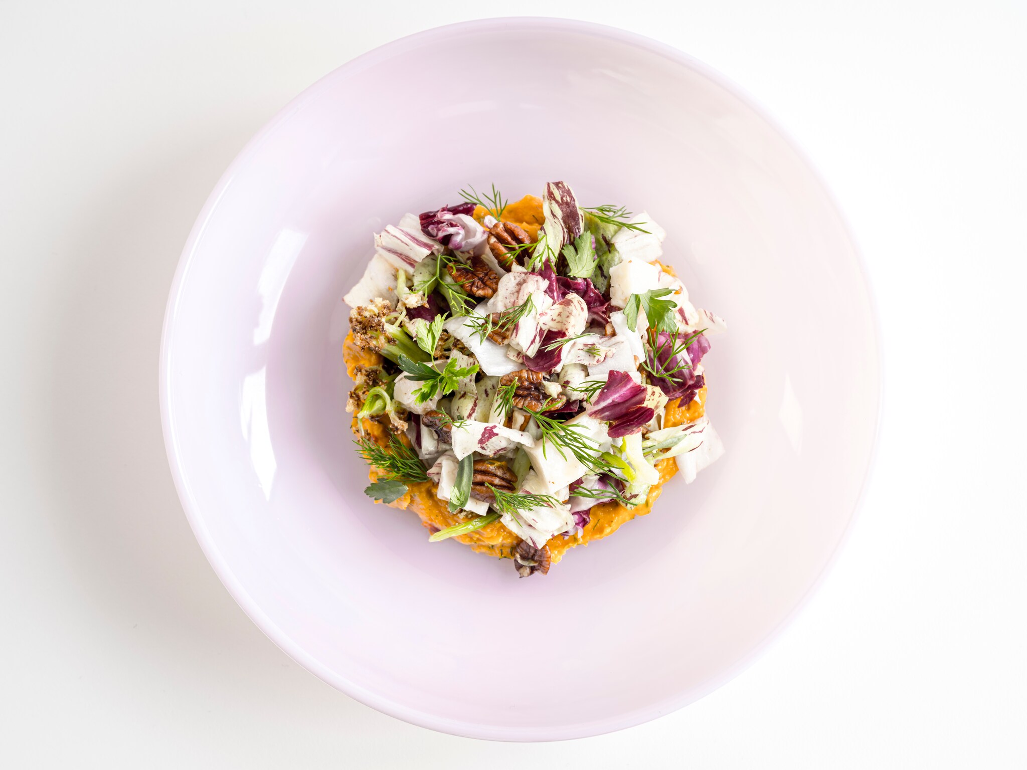 Overhead view of a chop salad. There’s a thick layer of orange butternut dip, with chopped-up dill, chicories, and cauliflower piled on top.