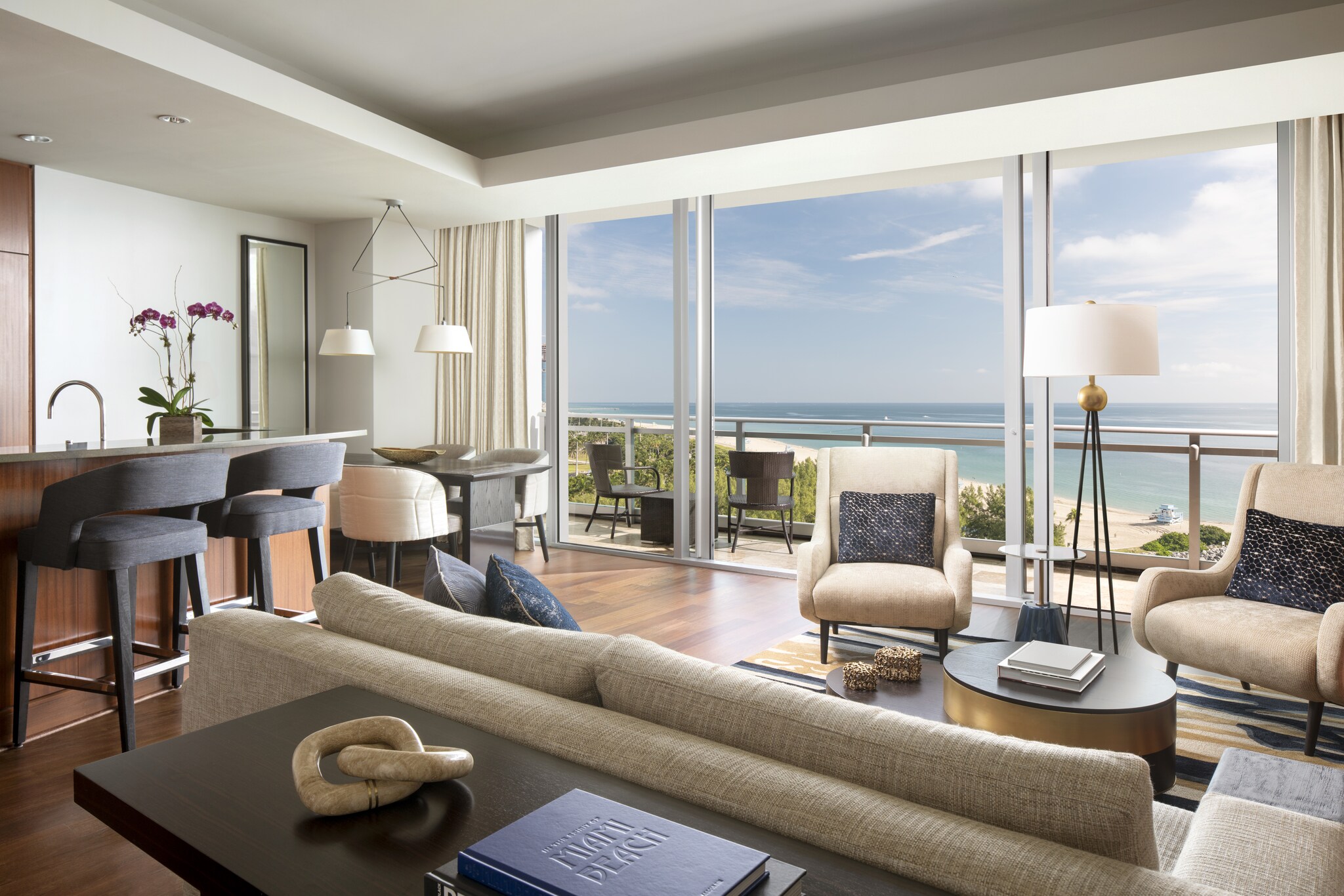 The common area of a suite features seating, a dining table, a kitchen, and sliding glass doors onto a private balcony.