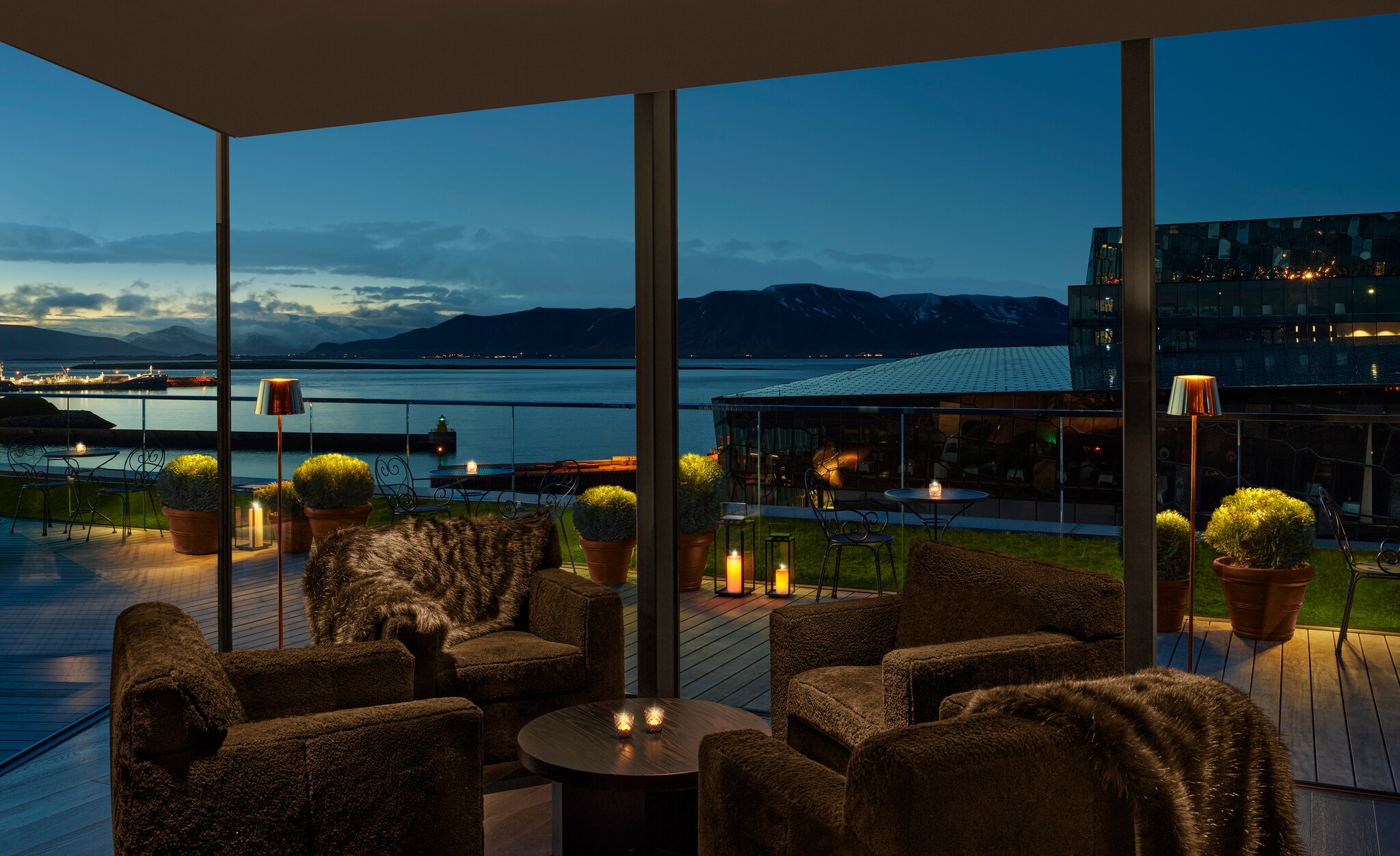 Inside the ROOFtop bar, brown armchairs are draped with fur blankets. Outside the floor-to-ceiling windows, a terrace overlooks the harbor.