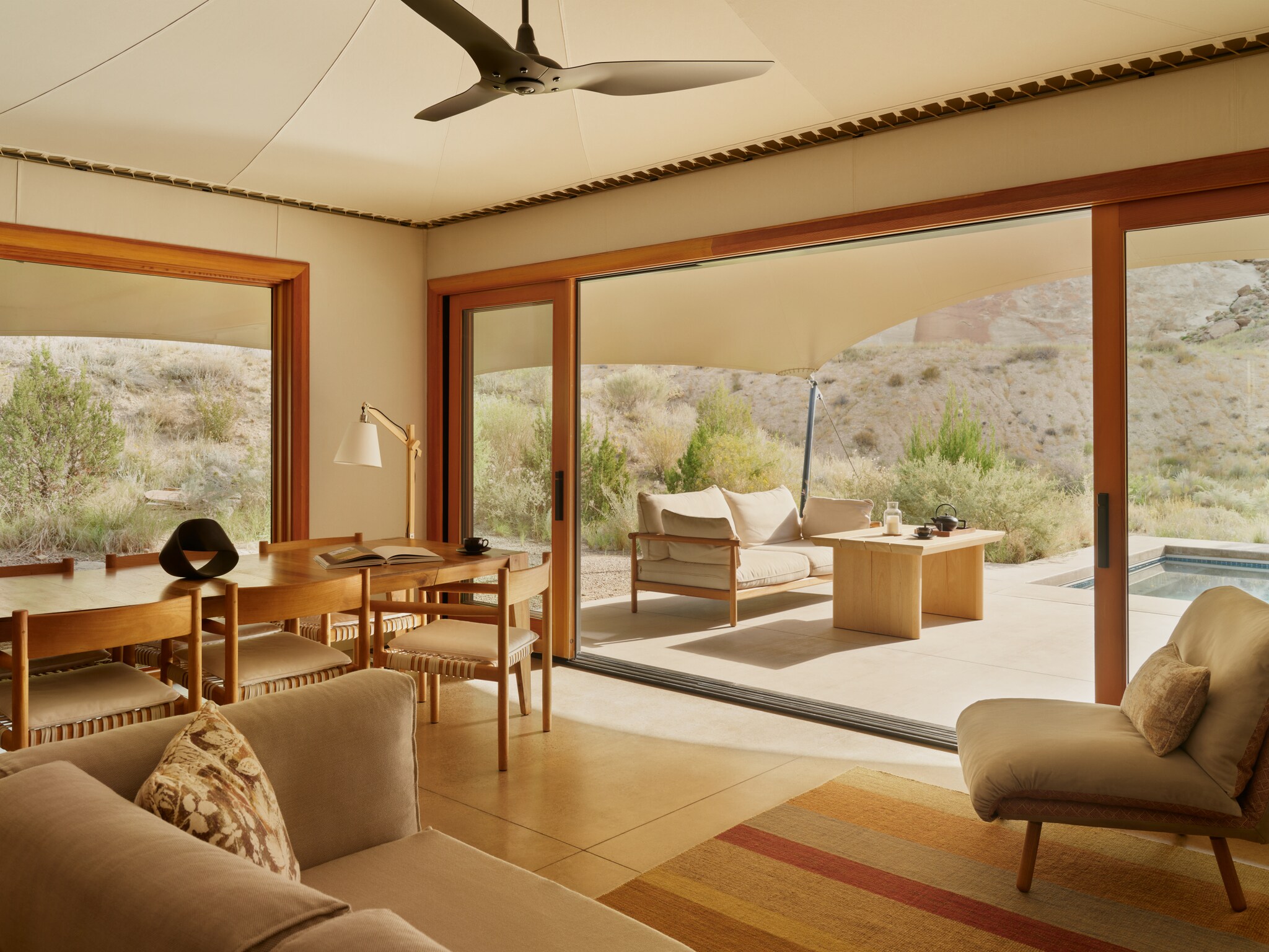 The living area of a One-Bedroom Mesa Pavilion is breezy and shady. Out the wide doors to the patio, a small plunge pool is visible.