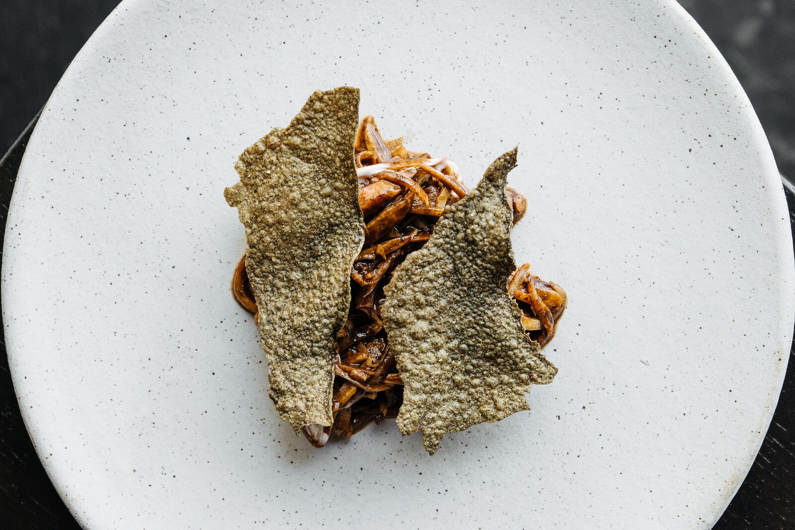 On a big, flecked white dish, a twirl of squid and asparagus in a red-brown sauce is topped with crispy, olive green chicharones.