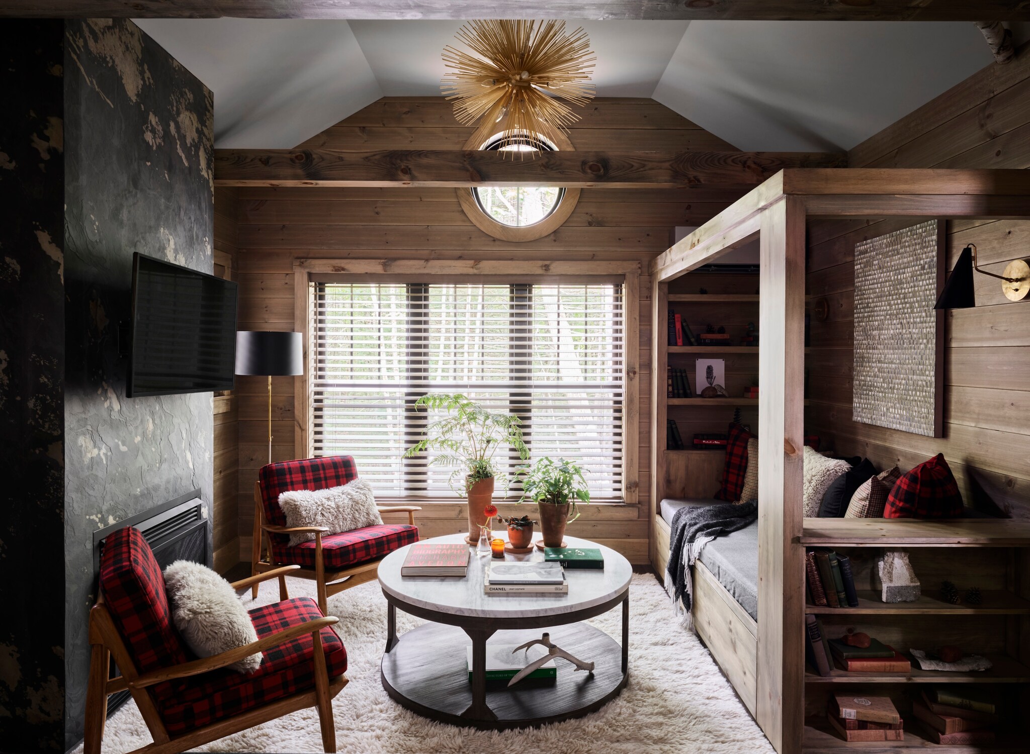 A small room has matte wood-paneled walls, chairs with red and black plaid cushions, and a small couch in a wooden frame with shelves.