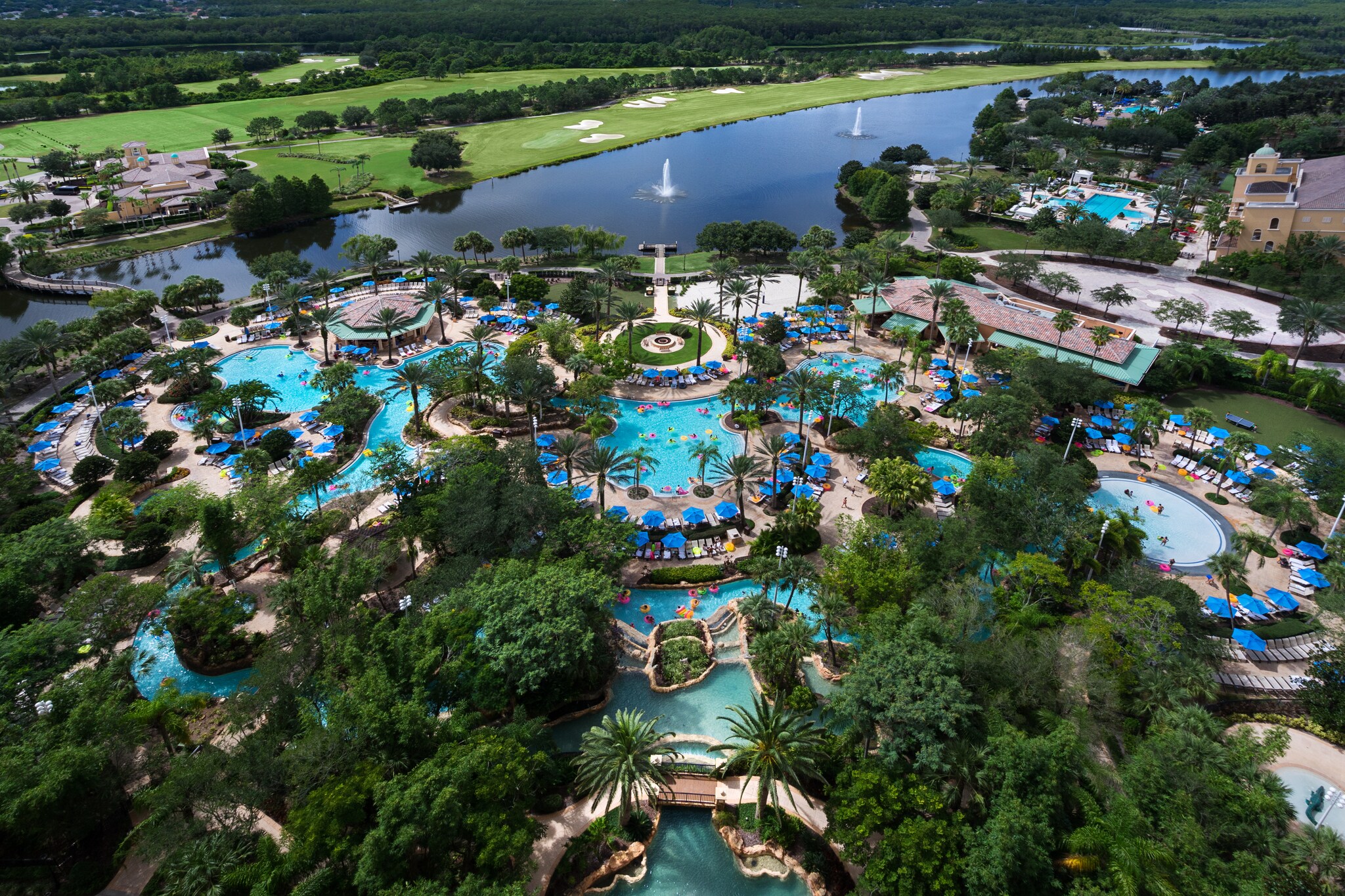 Aerial view of JW Marriott Orlando, Grande Lakes. Pools and lazy rivers wind through trees, and a big pond is dotted with fountains beyond.