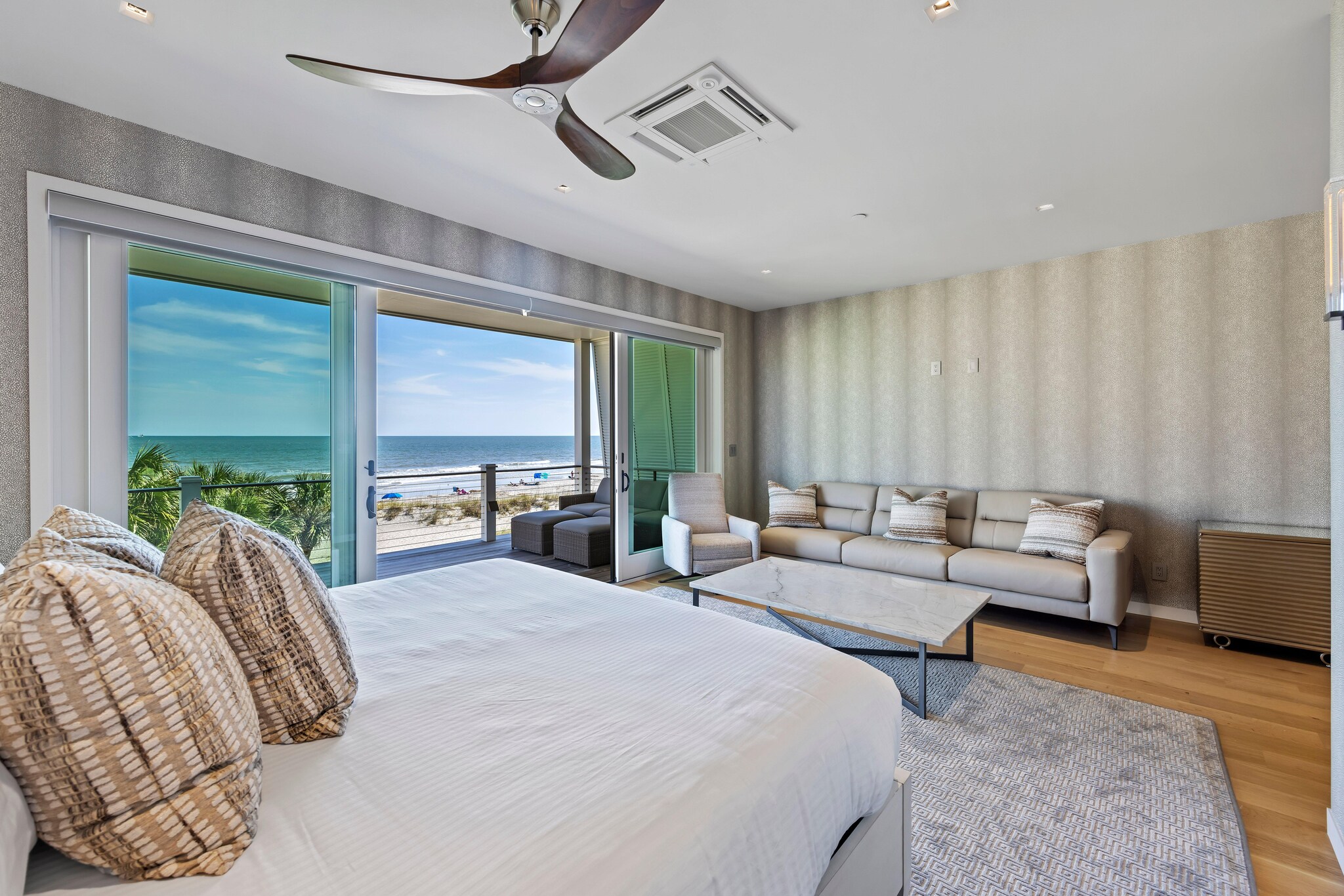Bright and airy bedroom featuring king bed and seating area with access to outdoor patio through large sliding door and view of the ocean.