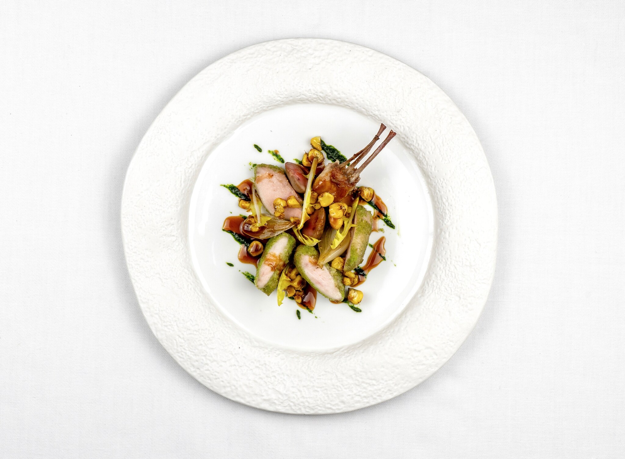 View from above a plate of roasted guinea fowl, encrusted with herbs and with a few slender bones sticking off to the side.