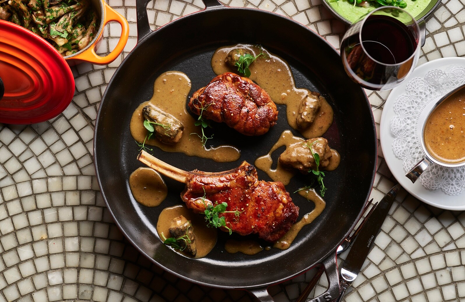 Overhead view of a circular black plate with a red veal chop and sweetbread drizzled with brown morel sauce.
