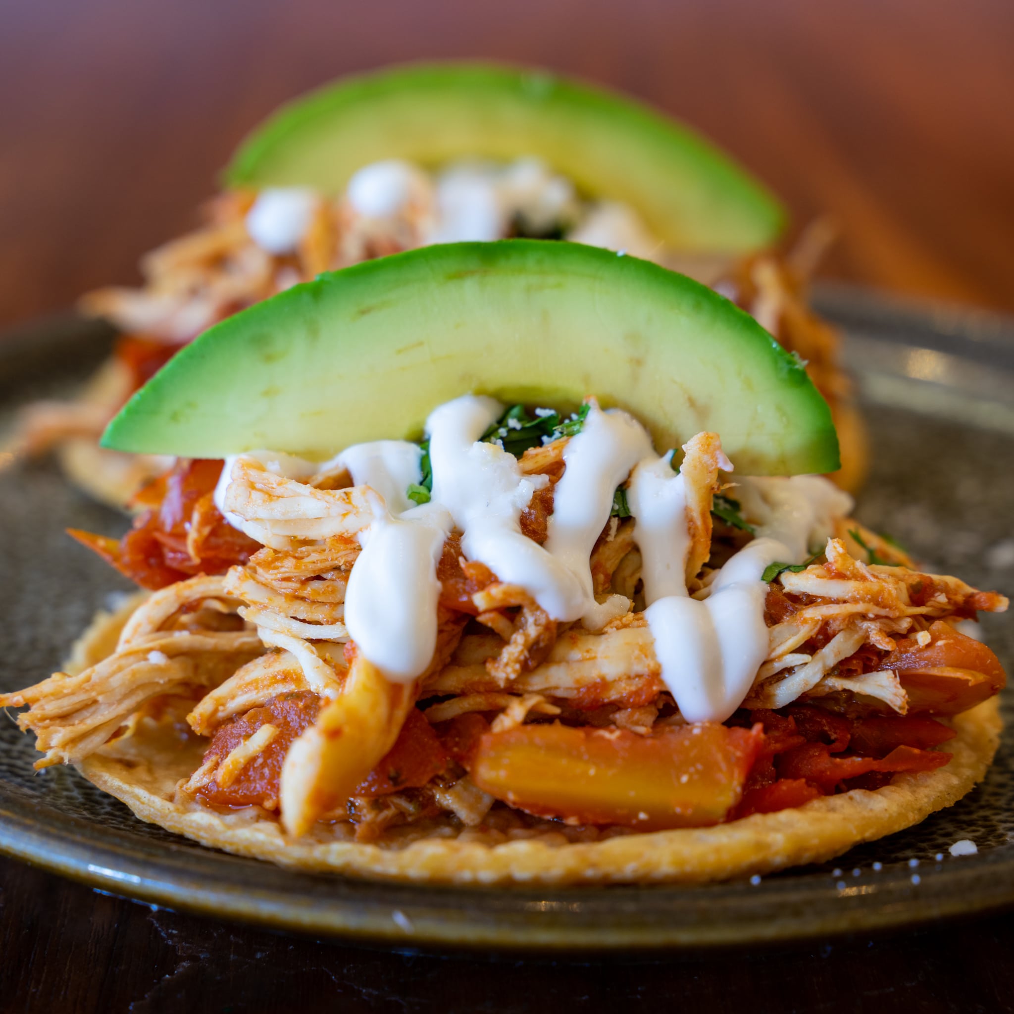Close-up of chicken tinga tacos, drizzled with crema and topped with a wedge of avocado.