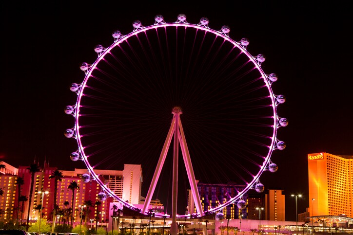 At night, the High Roller ferris wheel is lit in magenta light and towers above the surrounding hotel skyscrapers.