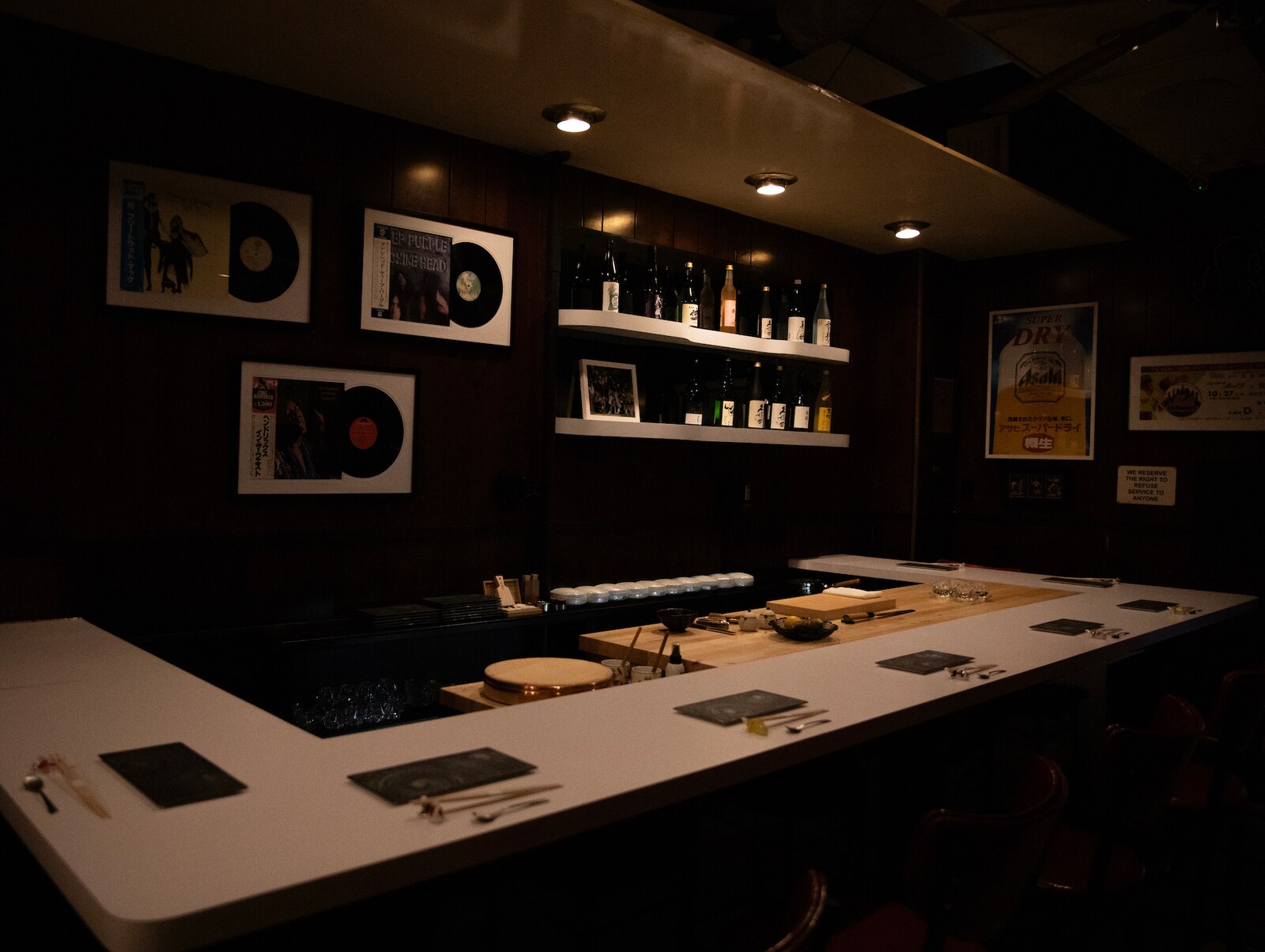 The bar at Sushi Oku is dim, with vinyl records mounted on the wall and a cutting board behind the white counter for preparing food.