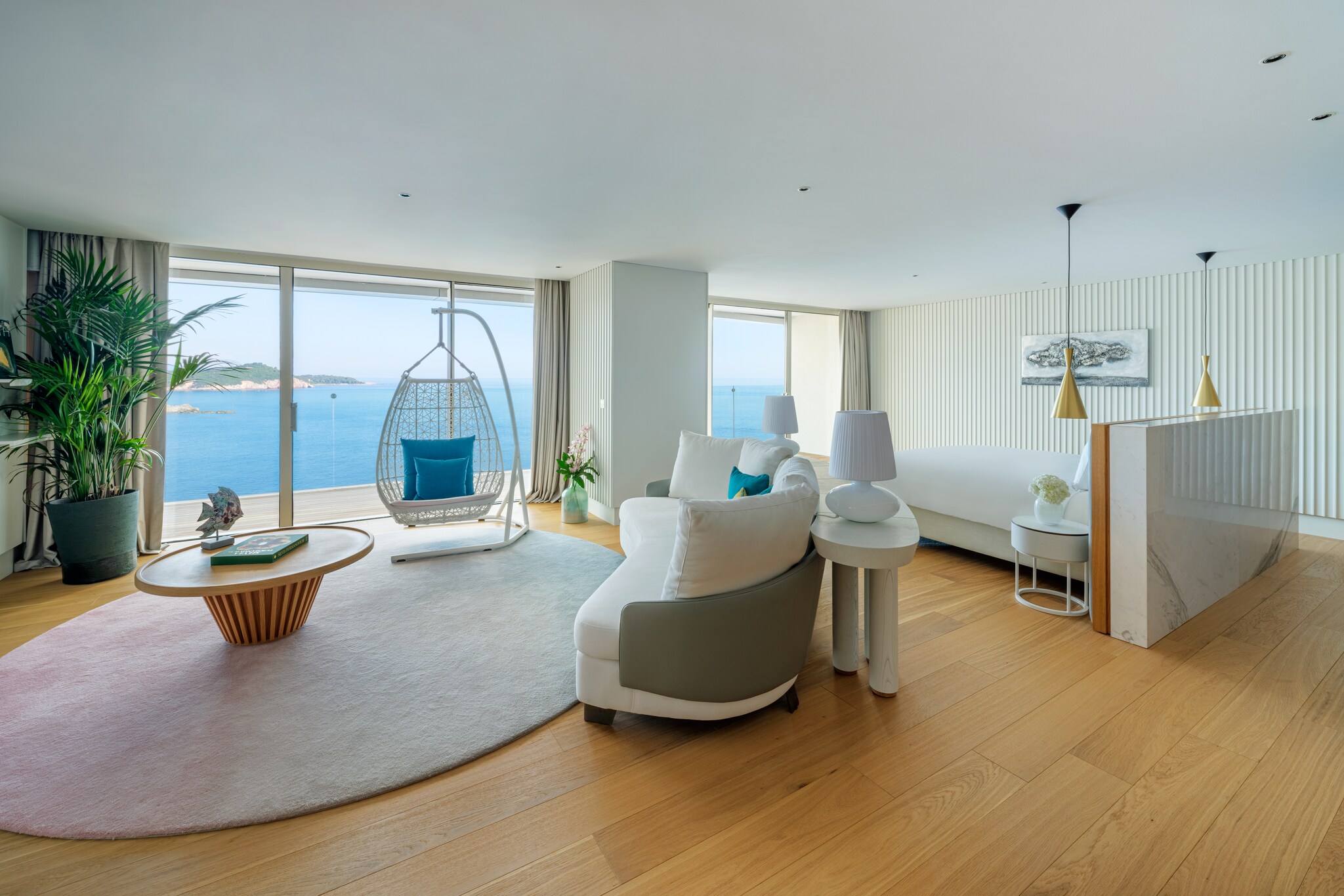 The living area of the Presidential Suite is roomy with white walls, a white basket chair, and a wall of glass looking out on the water.