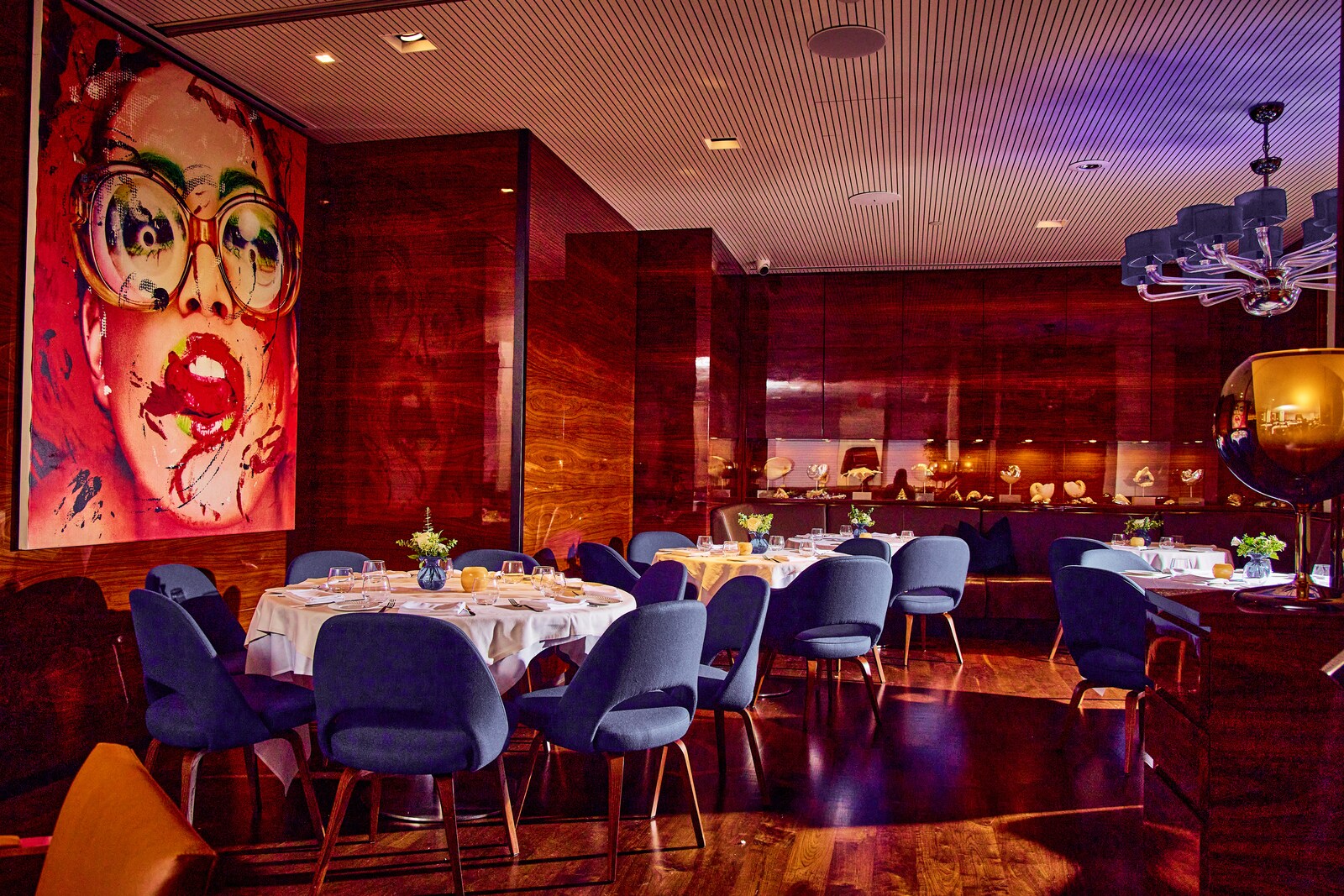 In Marea, blue chairs crowd by round dining tables, and a large painting of a woman in glasses dominates one wall.