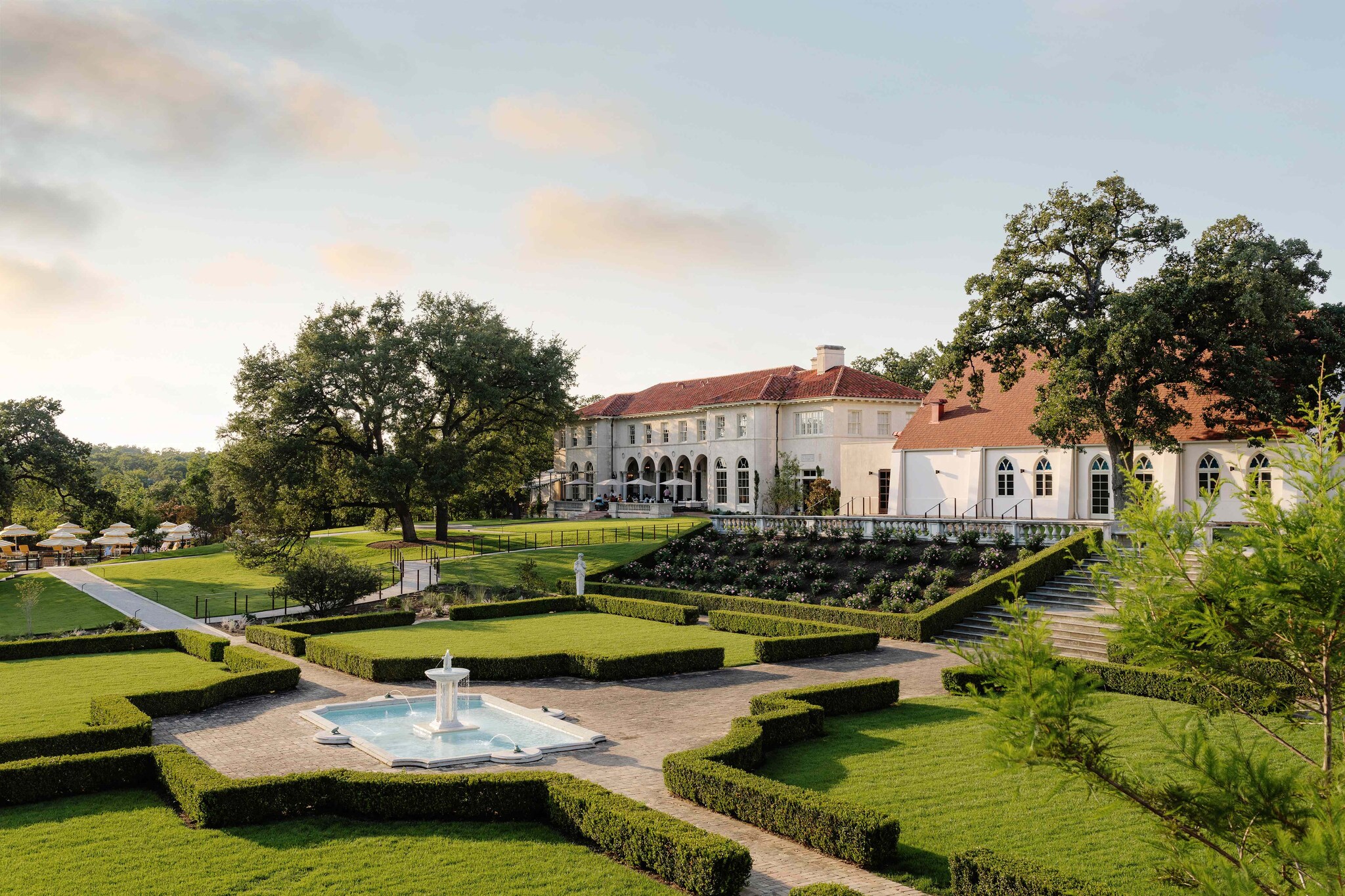 The terracotta roofs and cream exteriors of the Commodore Perry Estate are visible past manicured hedges, lawns, and a fountain.