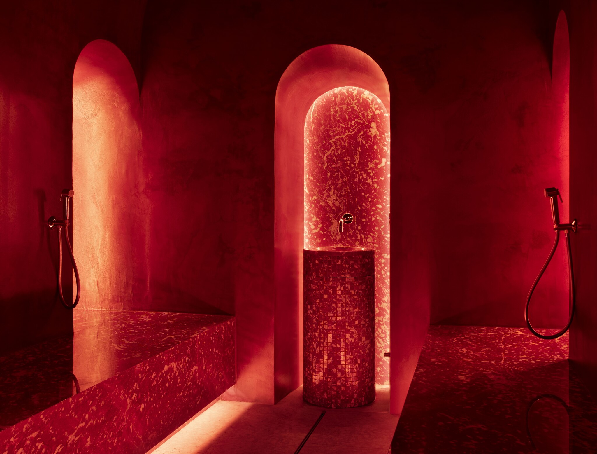 The arched doorways of a dark shower are lit with red and orange light.