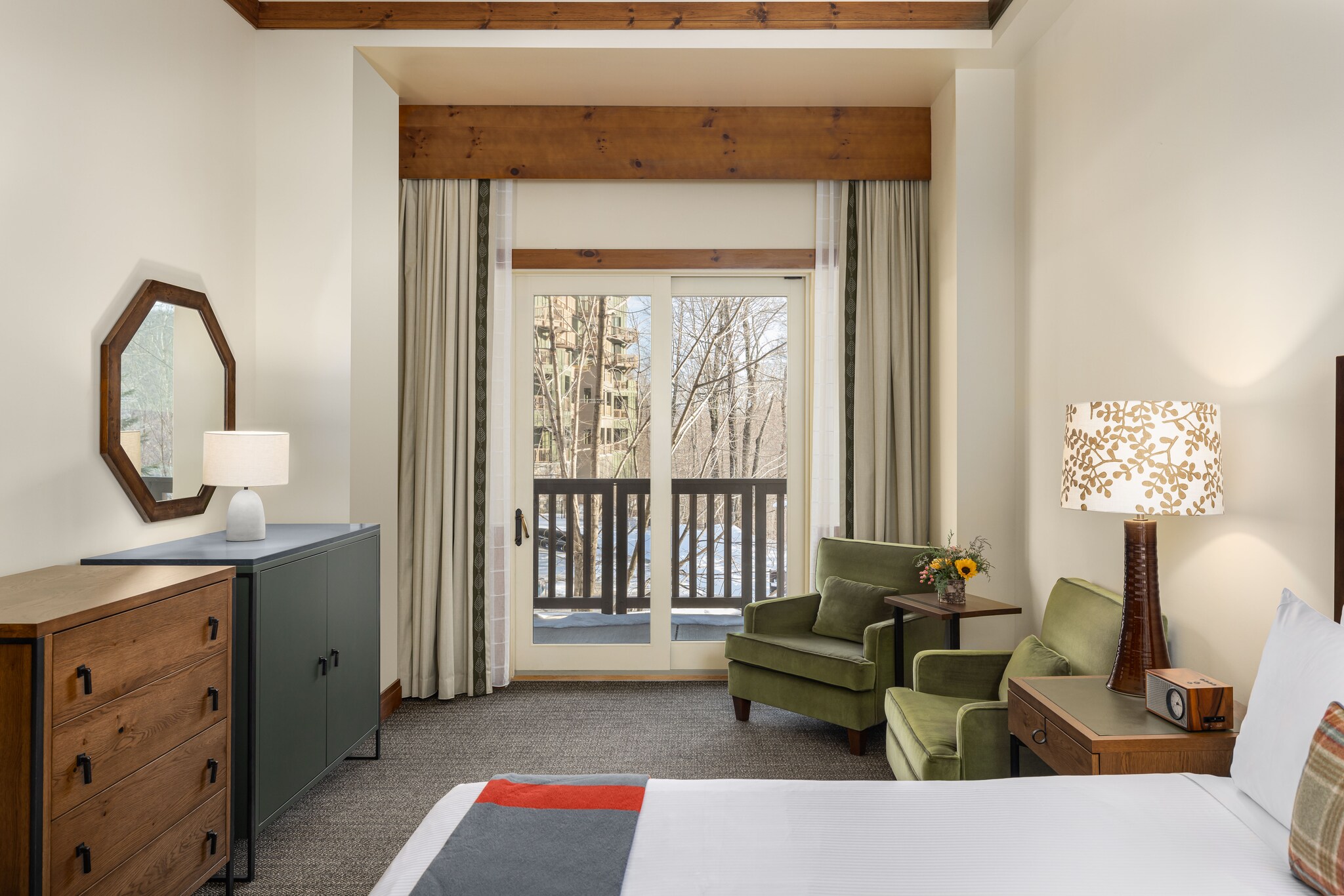 A Timberline Classic room has natural wood accents, green velvet chairs, and an octagonal mirror. Glass doors open onto a balcony.