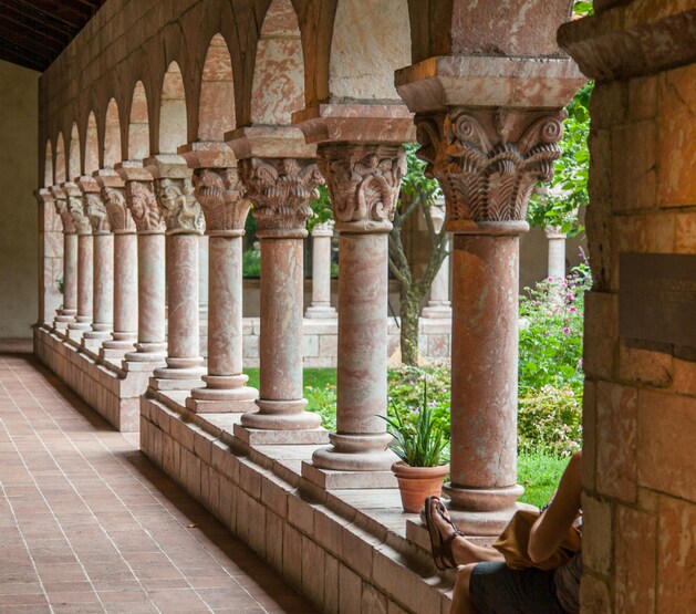 The Cuxa cloisters are carved from pink marble, with pillars, capitals, and carved grotesques. Beyond, the courtyard garden grows lush.