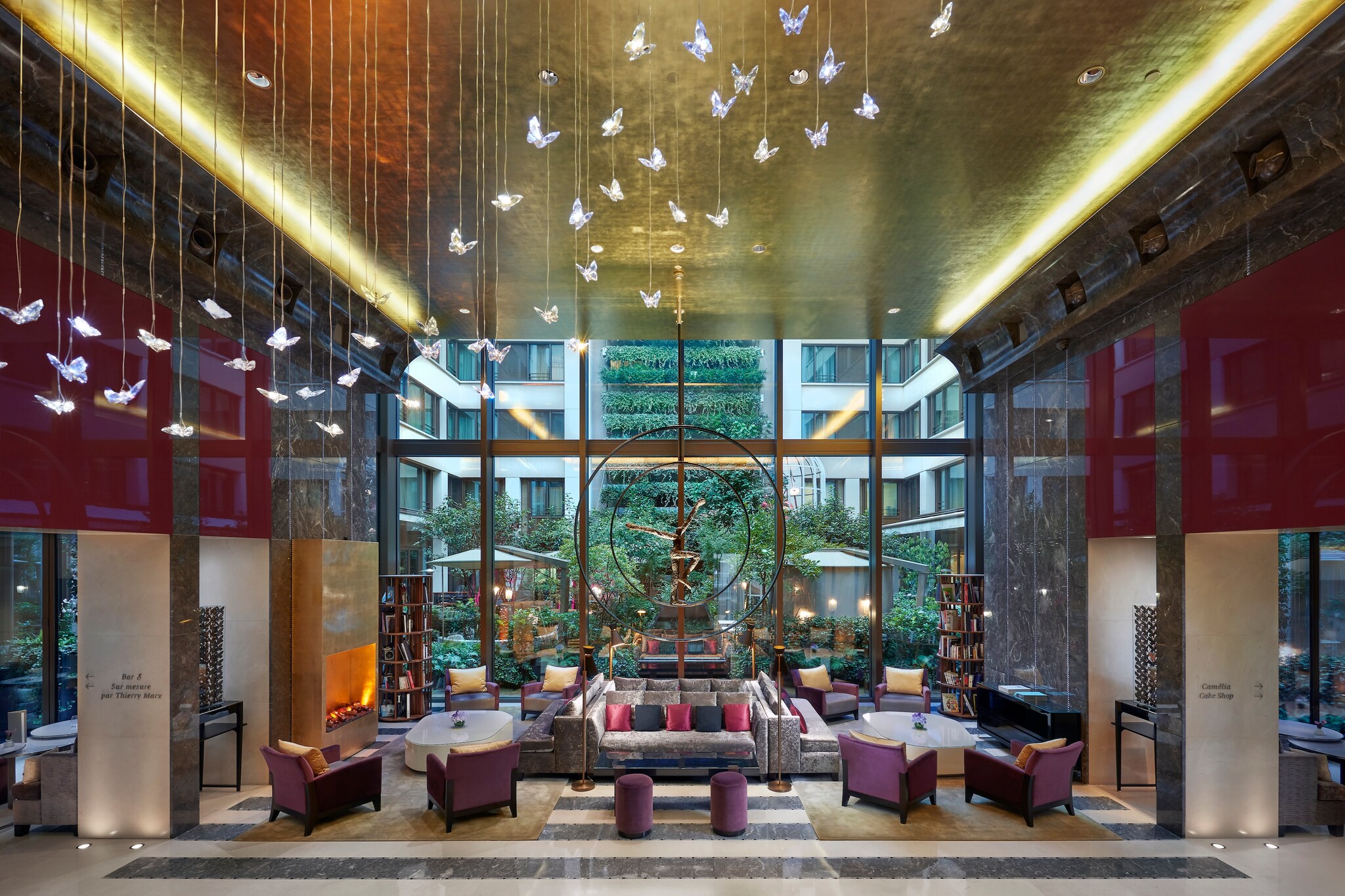 In the hotel lobby, butterfly-shaped lights hang from a gold ceiling. Couches and chairs offer seating next to a fireplace and bookshelves.